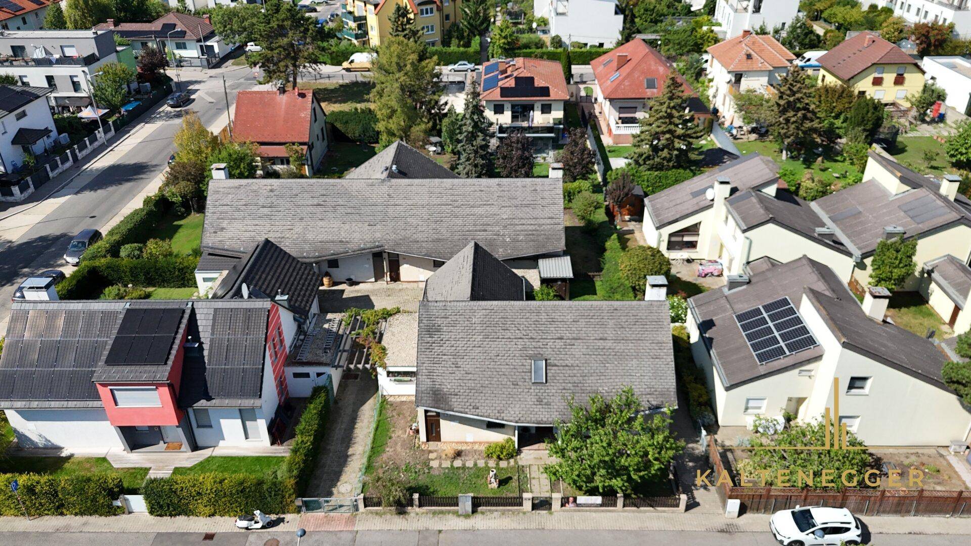 Weitläufige Luftaufnahme einer Wohnsiedlung mit Einfamilienhäusern, Gärten und grünen Straßenrändern.