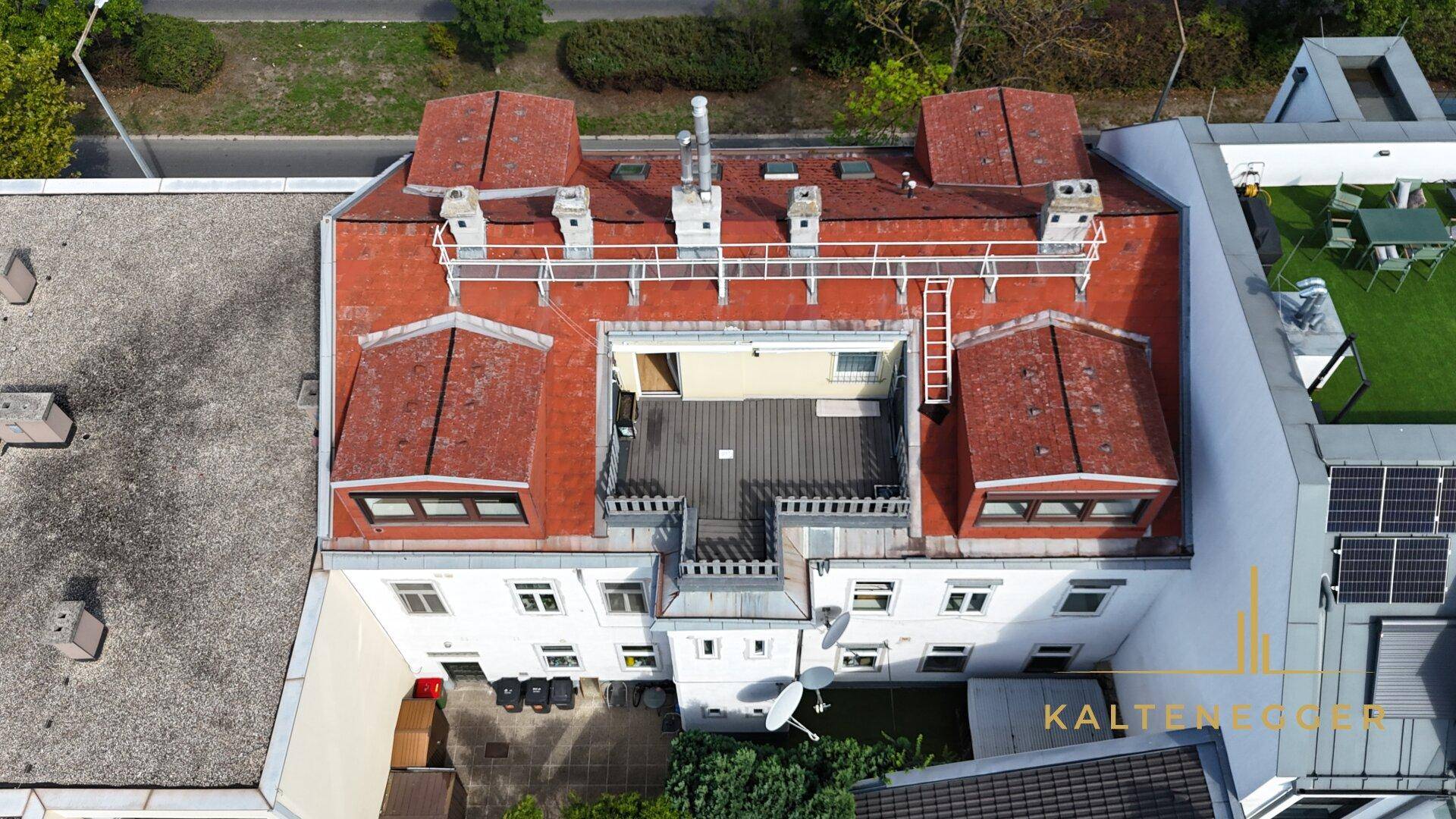 Luftaufnahme eines Gebäudes mit rotem Ziegeldach und einer zentralen Dachterrasse.