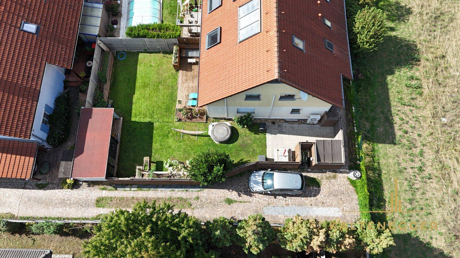 Weitläufige Luftaufnahme des Hauses mit Garten, Zufahrt und angrenzenden Feldern unter blauem Himmel.