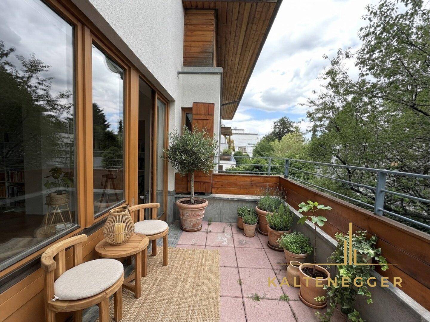 Möblierter Balkon mit Holzboden, Pflanzen und Blick auf die Umgebung.