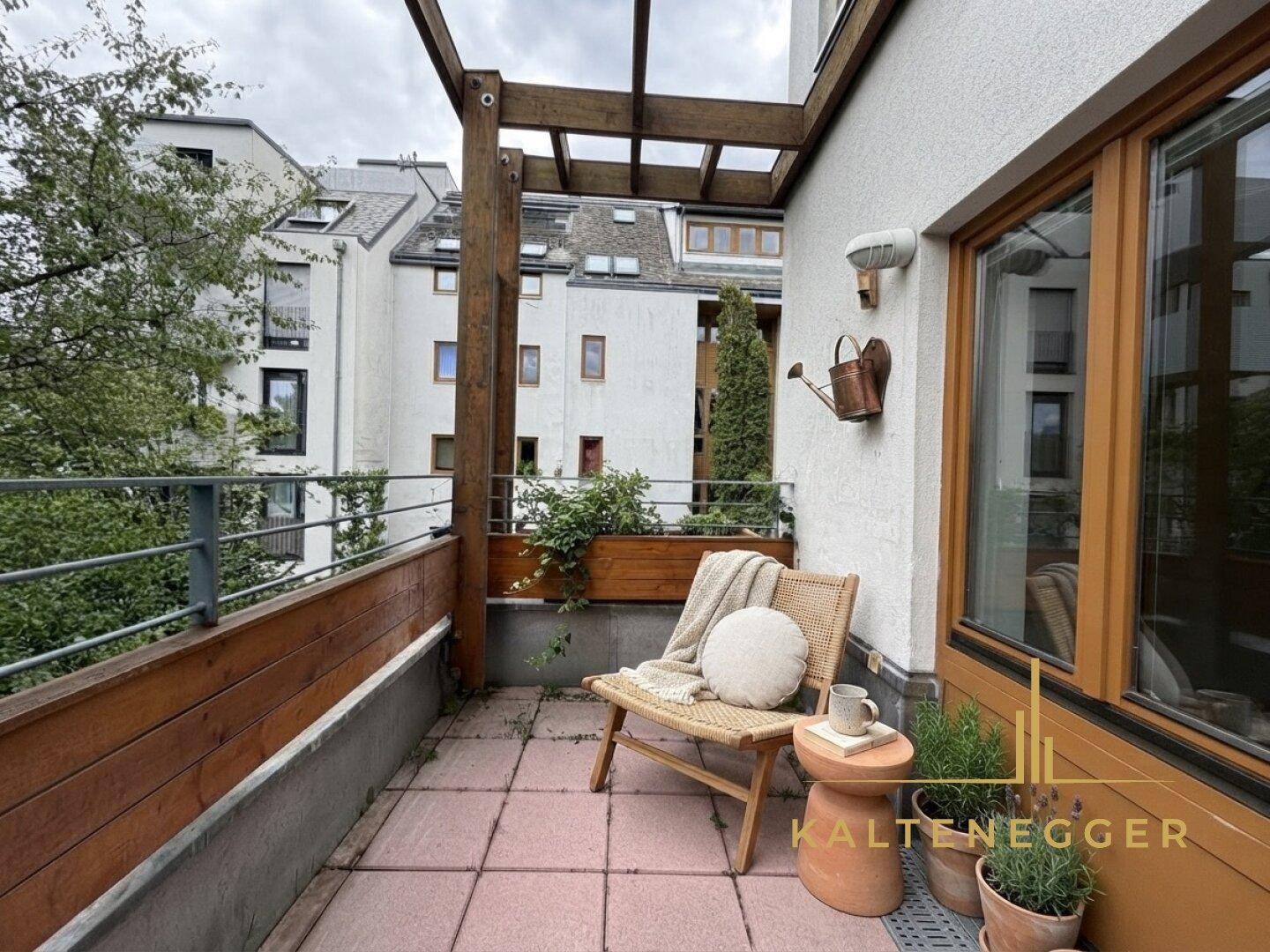 Kleiner Balkon mit Sitzgelegenheit, Pflanzen und Blick auf die umliegenden Gebäude.