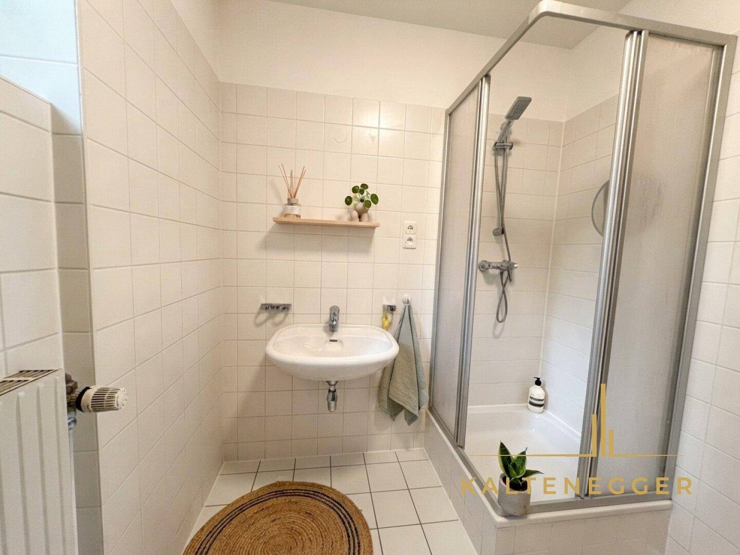 Kleines Badezimmer mit Dusche, Waschbecken und weißen Fliesen.