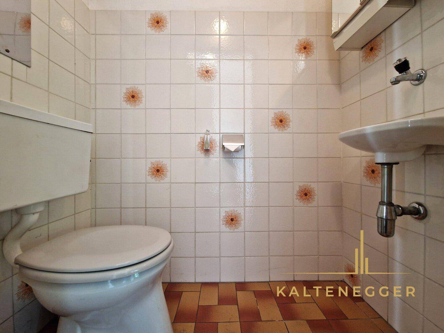 Kleines Gäste-WC mit gemusterten Fliesen, Toilette und Waschbecken.