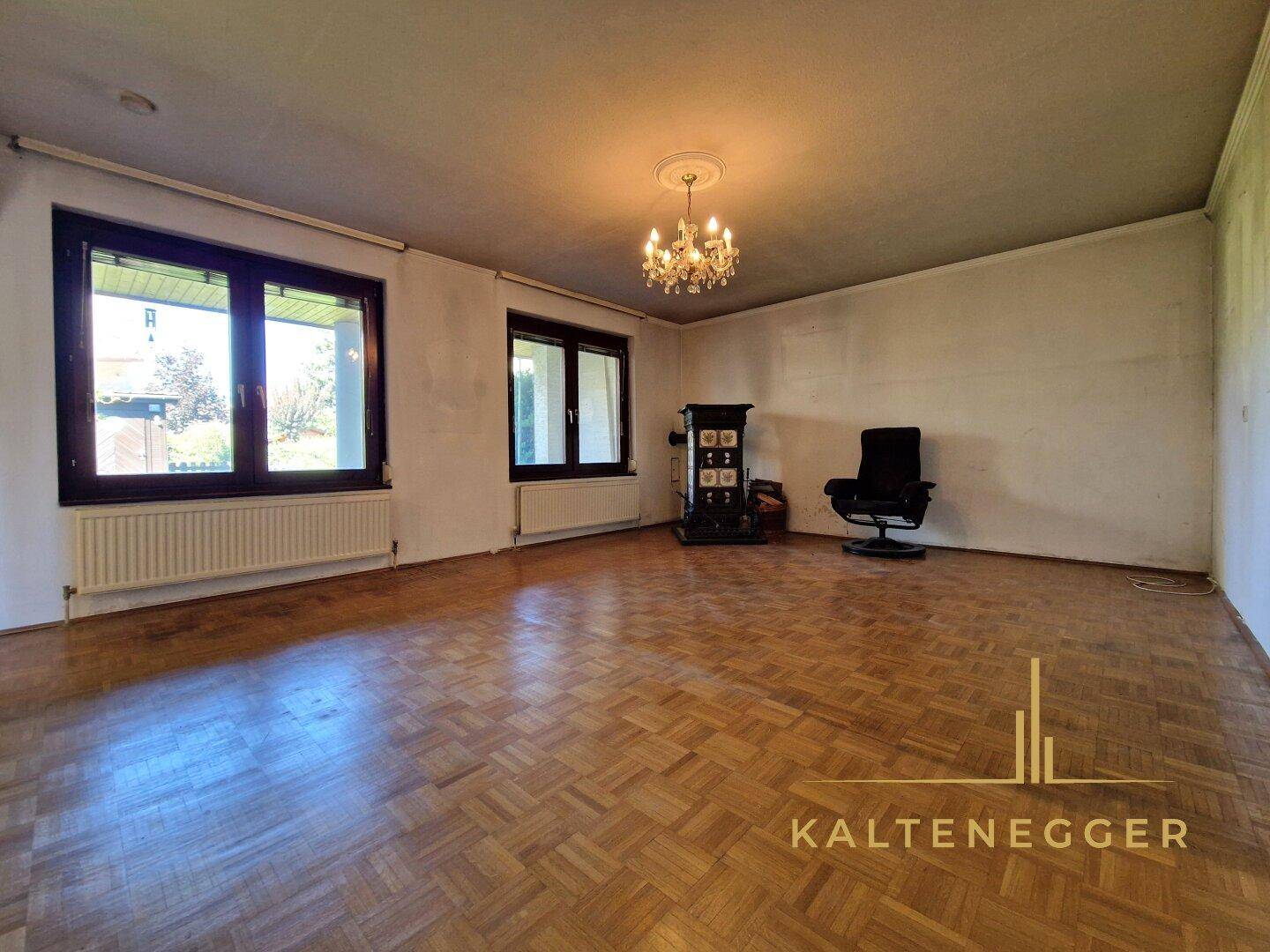 Geräumiges Wohnzimmer mit Parkettboden, großen Fenstern und Kronleuchter.