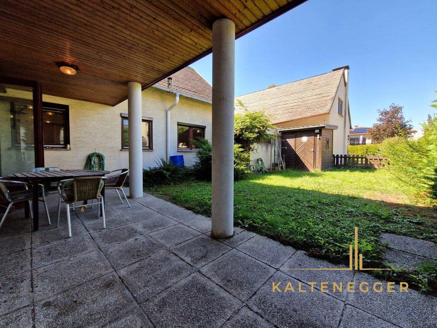 Überdachte Terrasse mit Steinfliesenboden und Gartenmöbeln, ideal für entspannte Stunden im Freien.