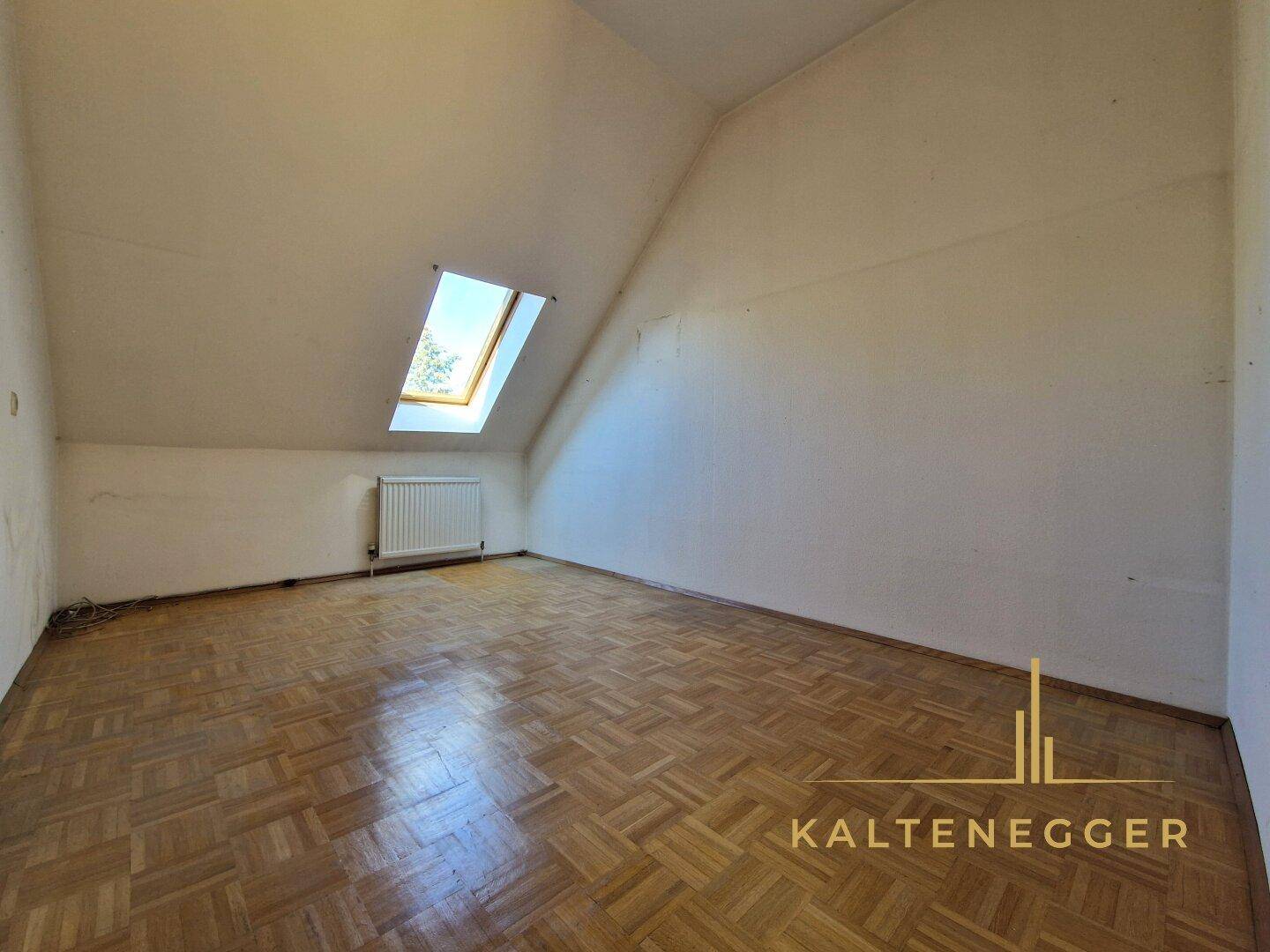 Geräumiger Dachgeschossraum mit Parkettboden, Dachschräge und Dachfenster.