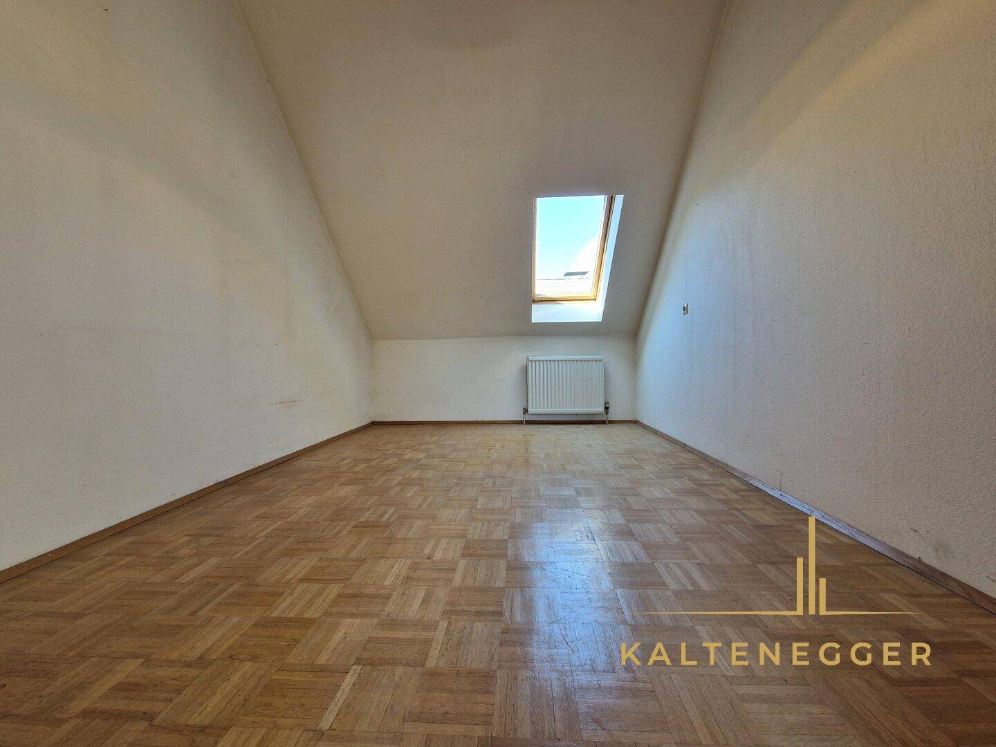 Heller Dachgeschossraum mit Parkettboden, Dachschräge und einem Dachfenster.
