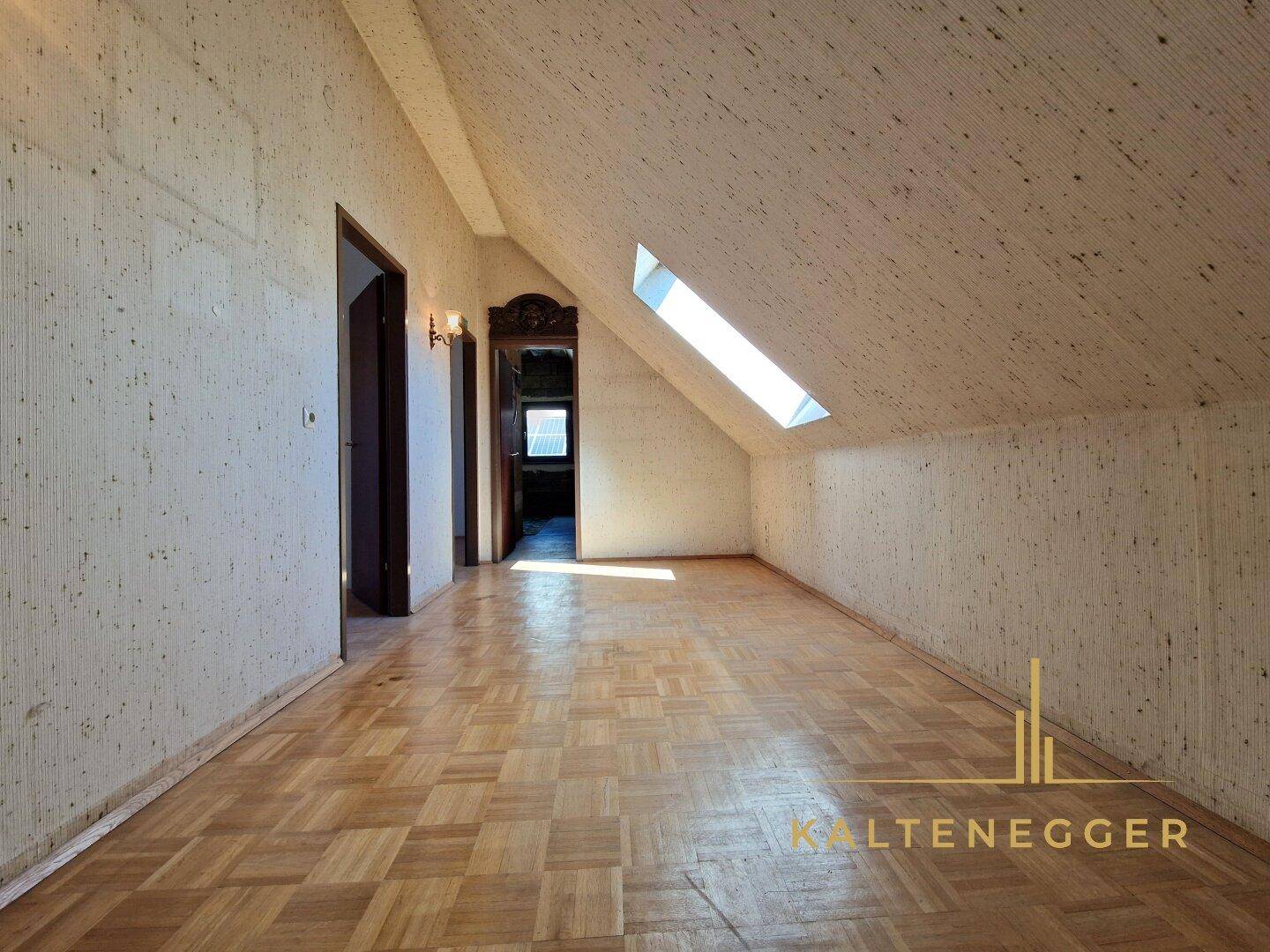 Dachgeschossraum mit Parkettboden, Dachschräge und Dachfenster für natürliches Licht.