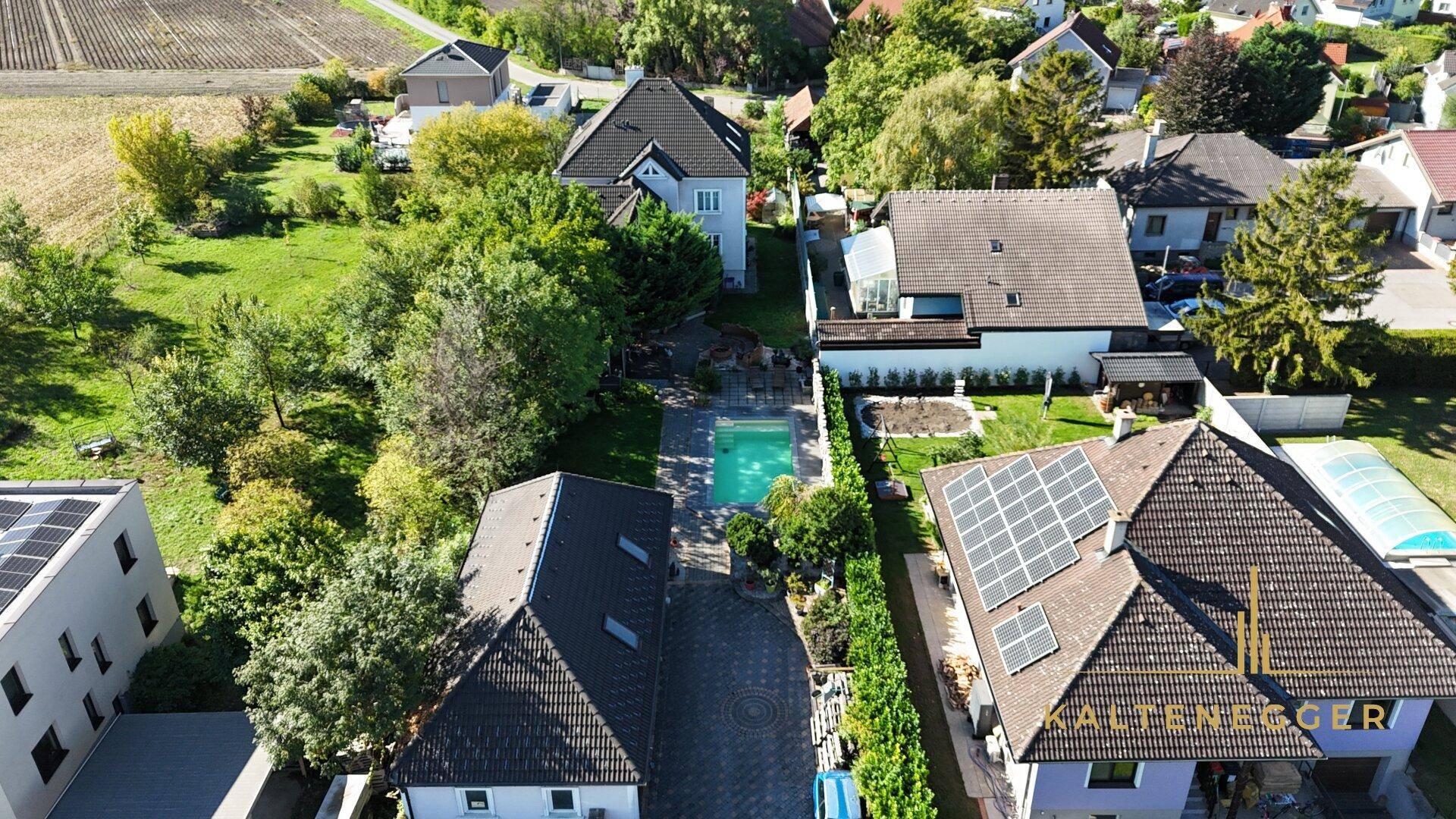 Luftaufnahme eines Anwesens mit Pool, gepflegtem Garten und umliegenden Häusern in ländlicher Umgebung.