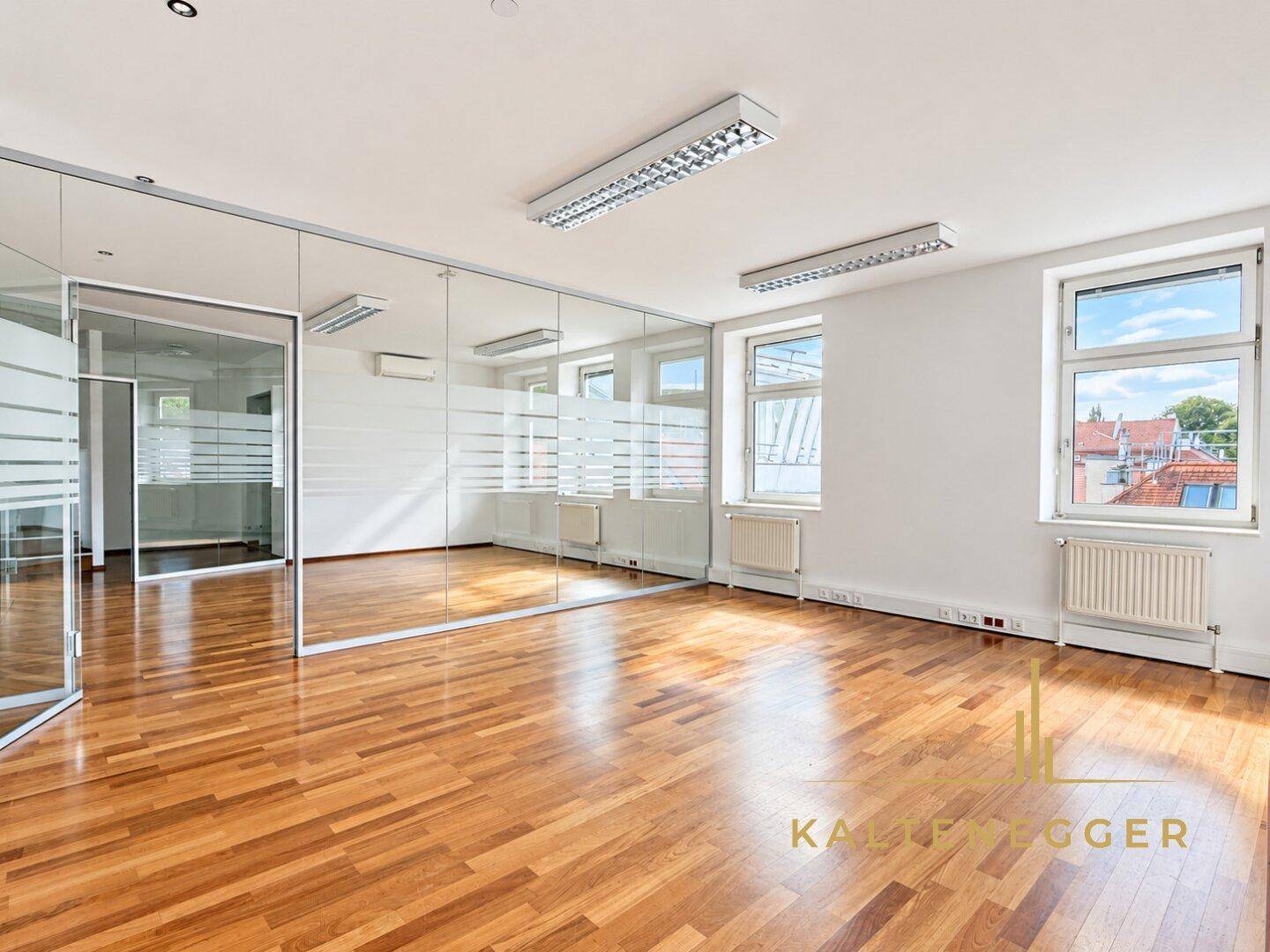 Helles Büro mit Holzboden, großen Fenstern und Glaswänden, die den Raum unterteilen.