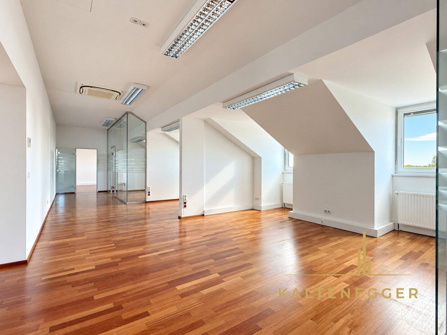 Geräumiges Büro mit Holzboden, Dachschrägen und großen Fenstern für viel Tageslicht.