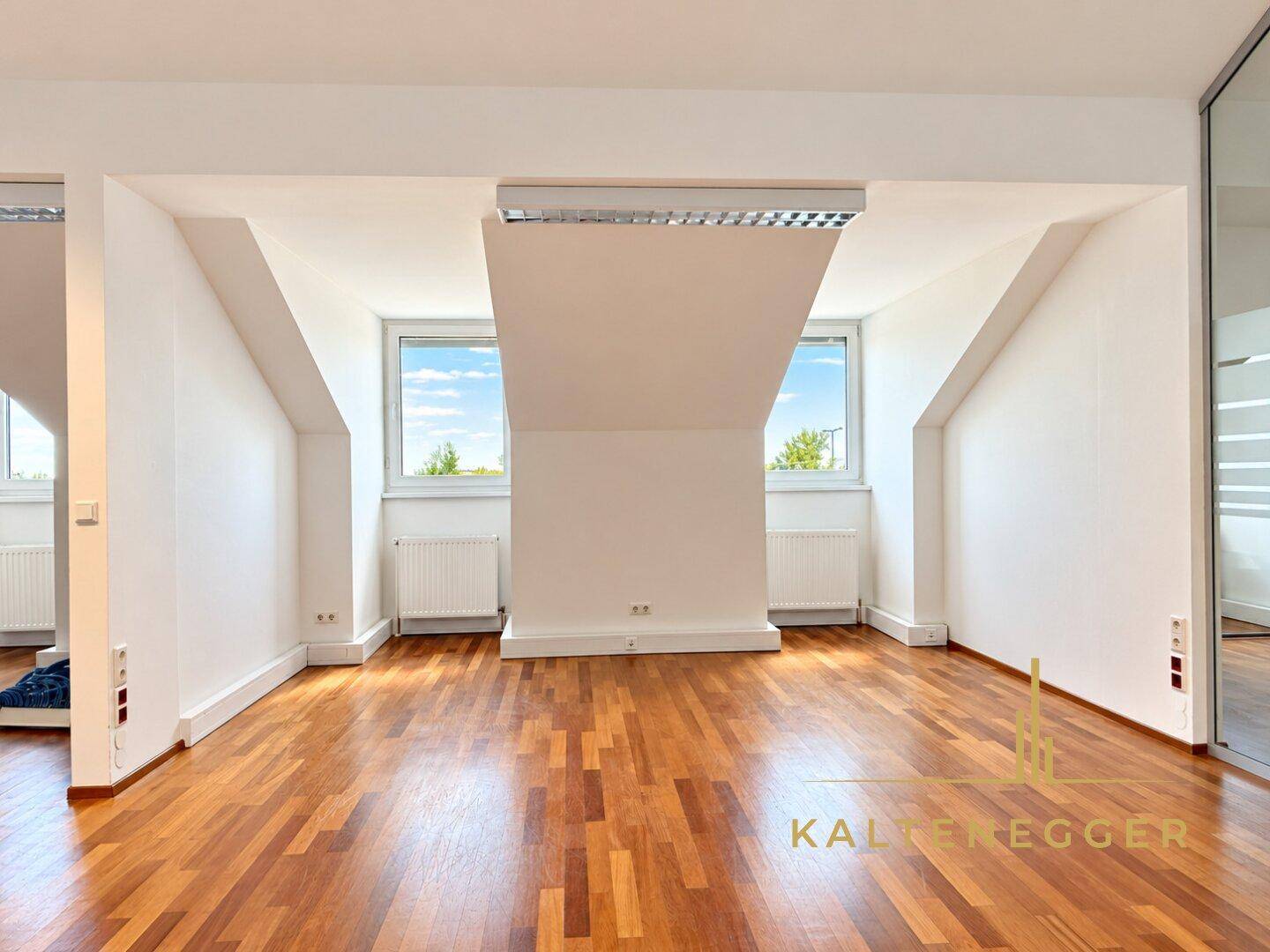 Helles Büro mit Holzboden, Dachschrägen und zwei großen Fenstern mit Ausblick.