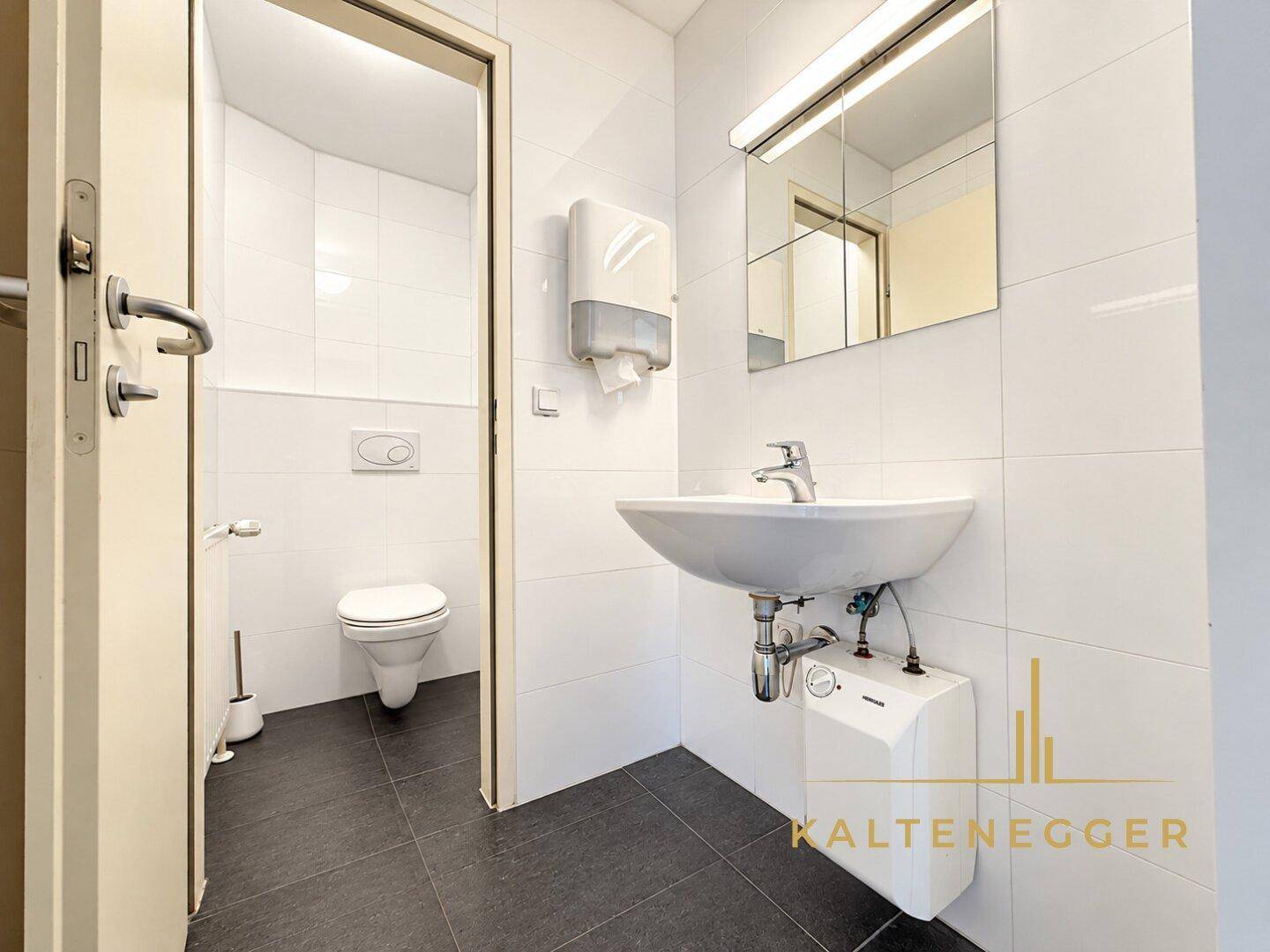 Saubere Gästetoilette mit weißen Fliesen, Waschbecken und Wand-WC.