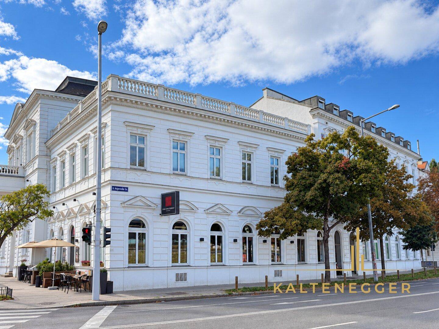 Elegantes weißes Gebäude an einer Straße mit Bäumen und blauem Himmel.