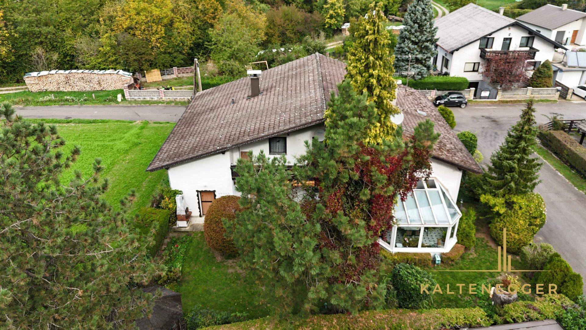 Seitenansicht des Hauses mit Wintergarten, umgeben von Bäumen und Grünflächen.