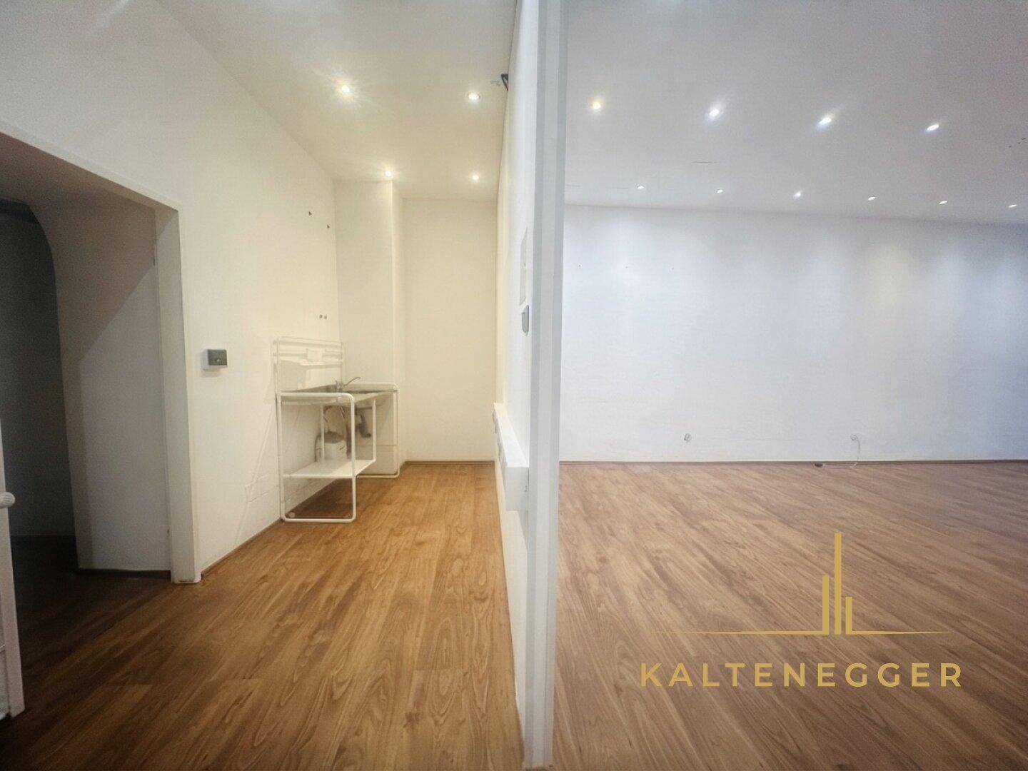 Blick von einem kleineren Bereich mit Waschbecken in einen größeren, leeren Hauptraum.