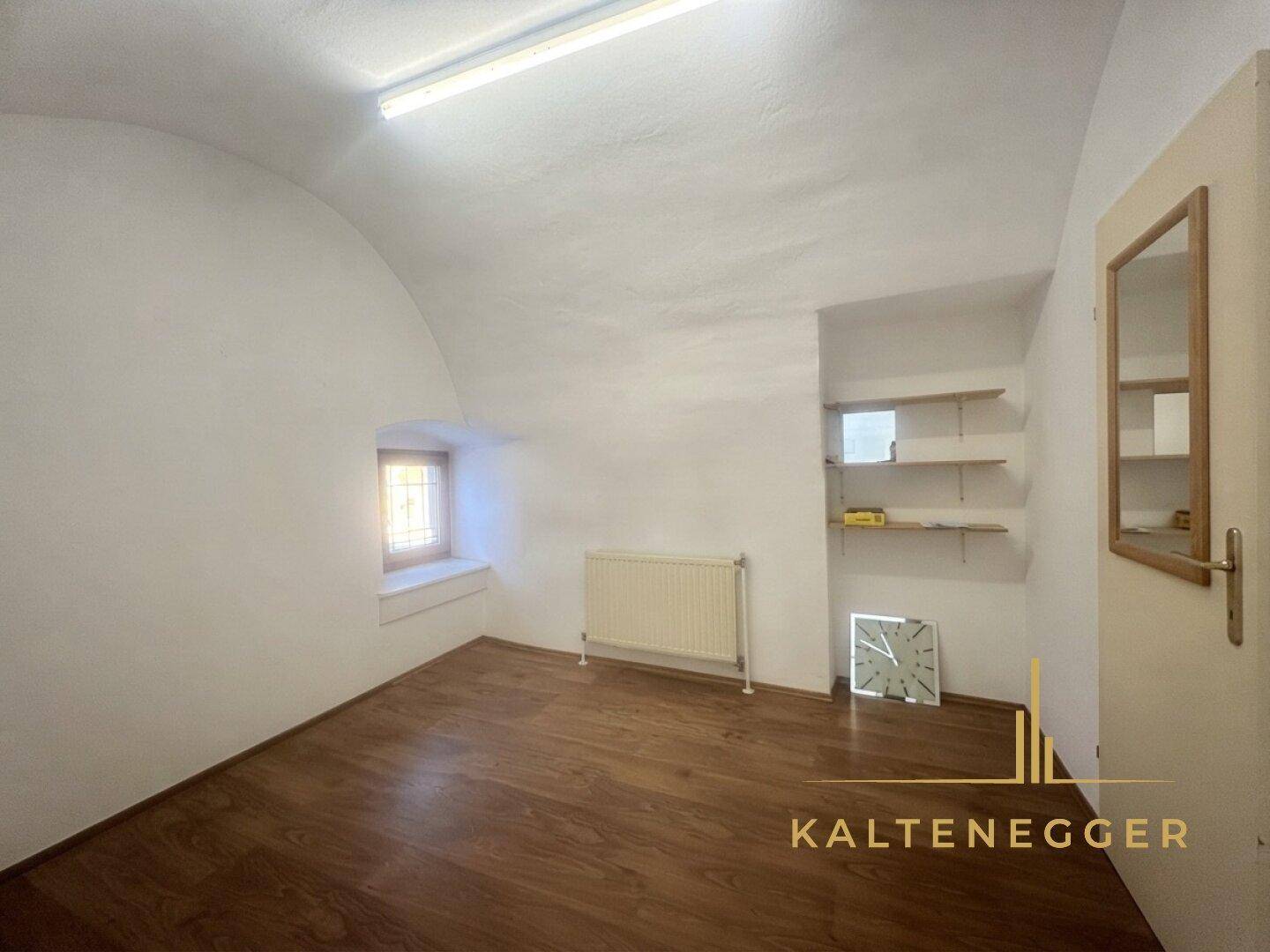 Raum mit gewölbter Decke, Laminatboden und einem kleinen Fenster, ideal als Lager oder Büro.