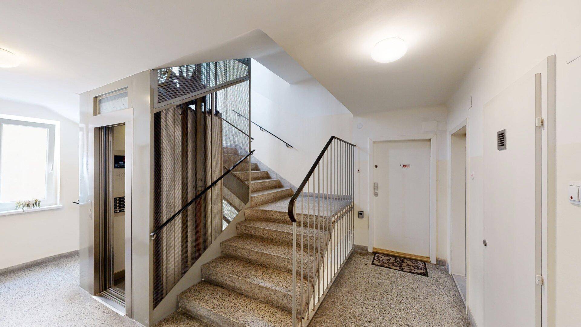 Treppenhaus mit Granitstufen und modernem Aufzug in einem Mehrfamilienhaus.