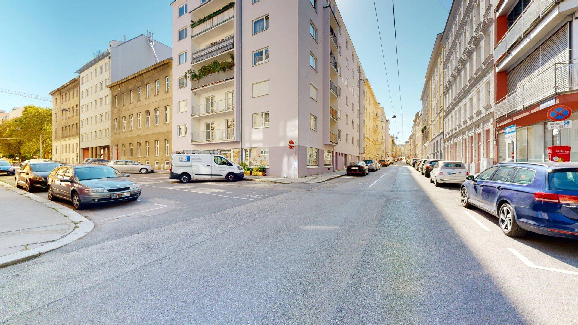 Straßenansicht eines modernen Wohngebäudes mit Balkonen und parkenden Autos.