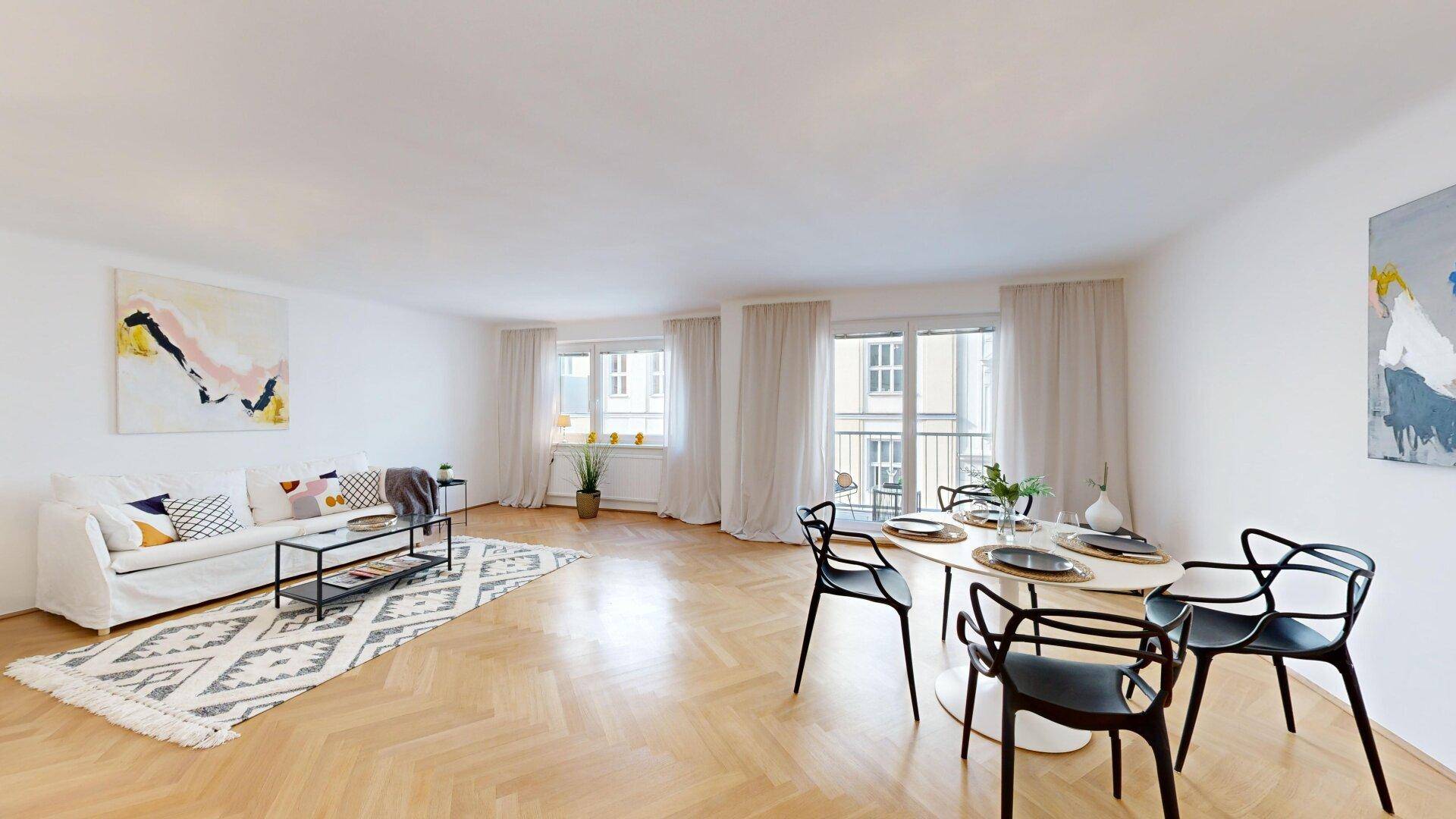 Heller Wohn- und Essbereich mit Fischgrätparkett, modernem Sofa und Zugang zu einem Balkon.