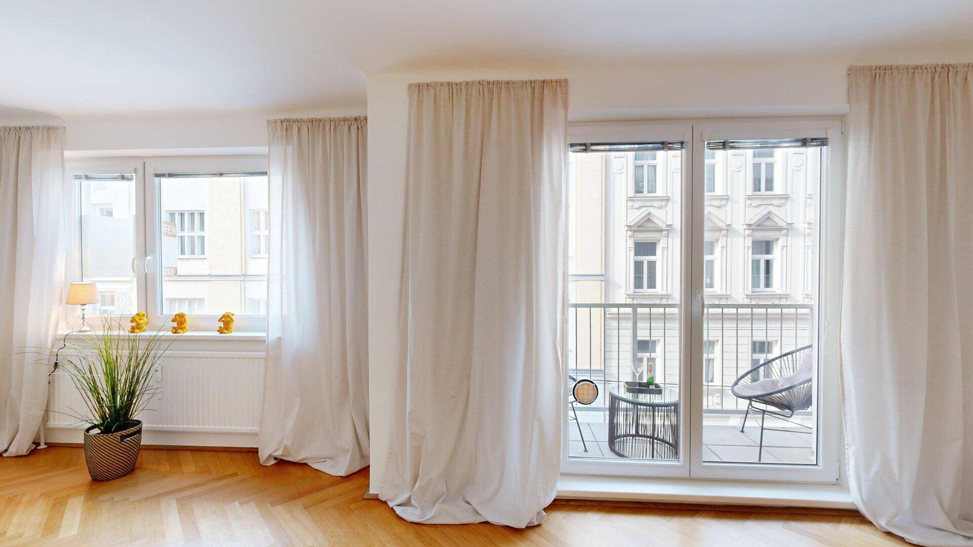Große Fensterfront mit Blick auf die gegenüberliegende Fassade und Zugang zu einem kleinen Balkon.