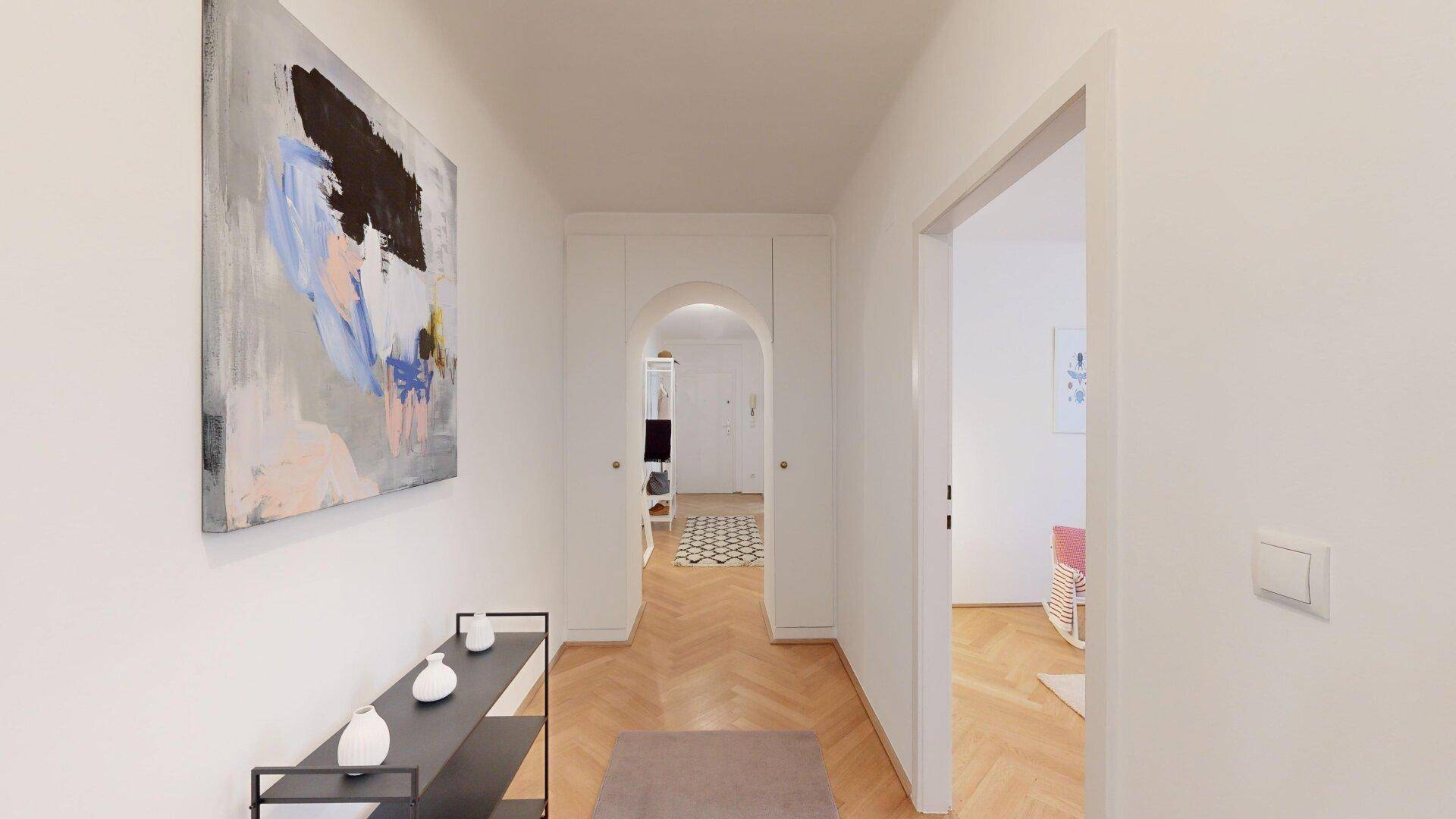 Langer Flur mit Fischgrätparkett, Kunst an der Wand und Zugang zu mehreren Räumen.