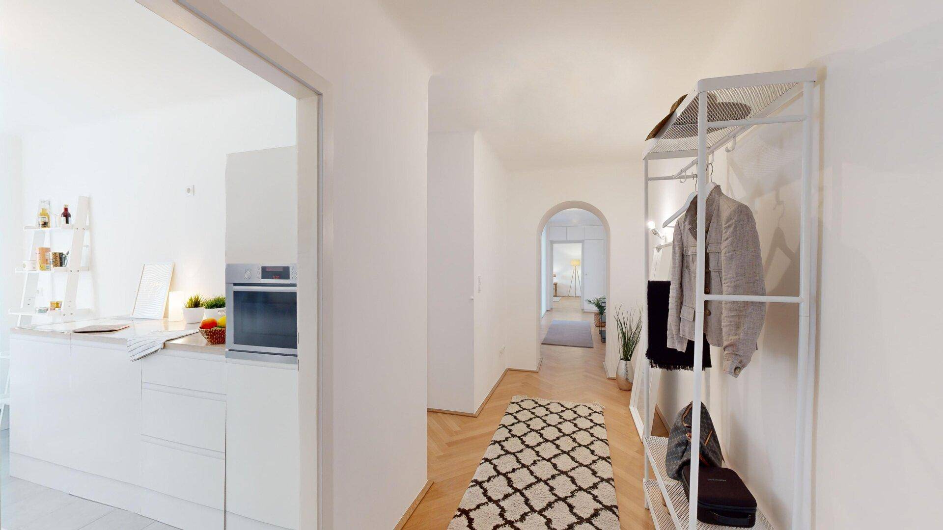 Eingangsbereich mit Garderobe, Fischgrätparkett und Blick in die angrenzende Küche.