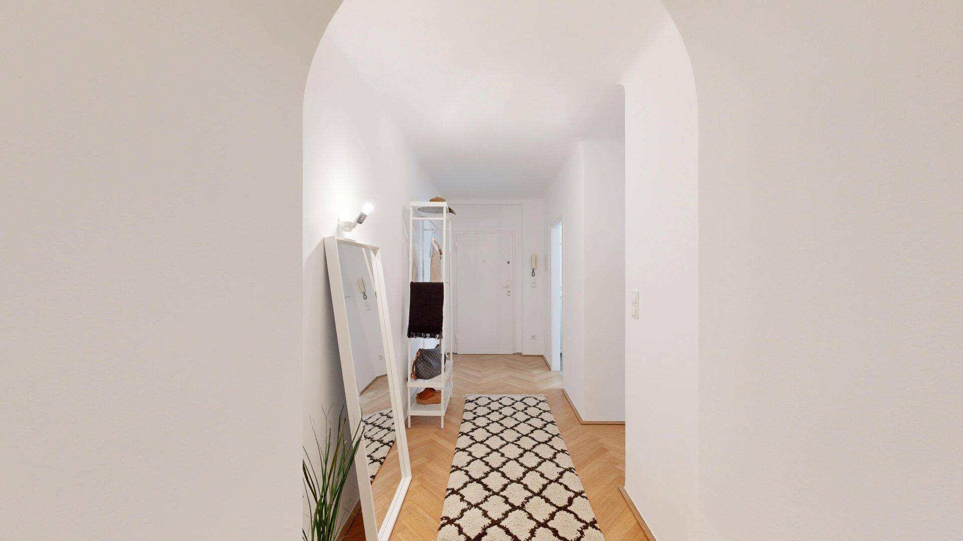 Heller Eingangsbereich mit Spiegel, Garderobe und Fischgrätparkettboden.
