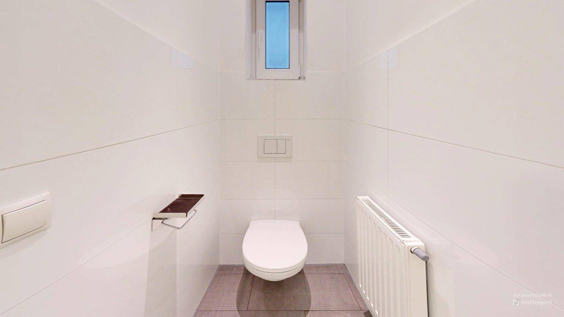 Saubere Toilette mit weißer Keramik, Fliesenwänden und einem kleinen Fenster.
