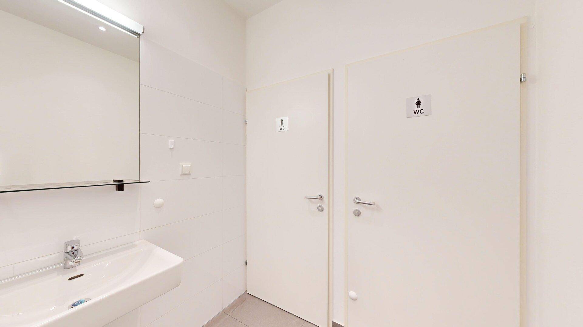 Moderner Waschraum mit Waschbecken und zwei separaten Toilettenkabinen.