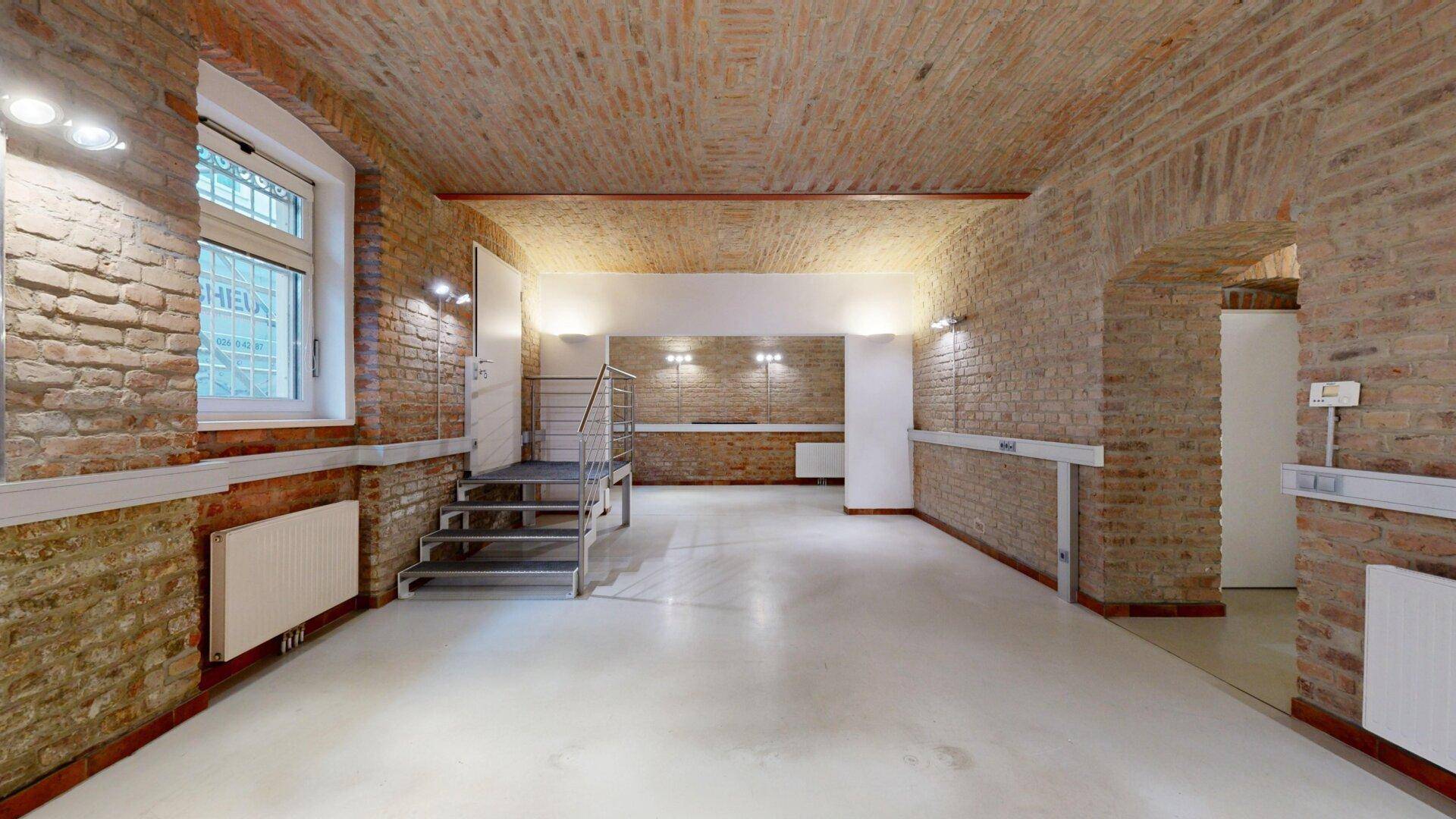 Geräumiger Büroraum mit Ziegelwänden, Gewölbedecke und einem erhöhten Bereich mit Treppe.