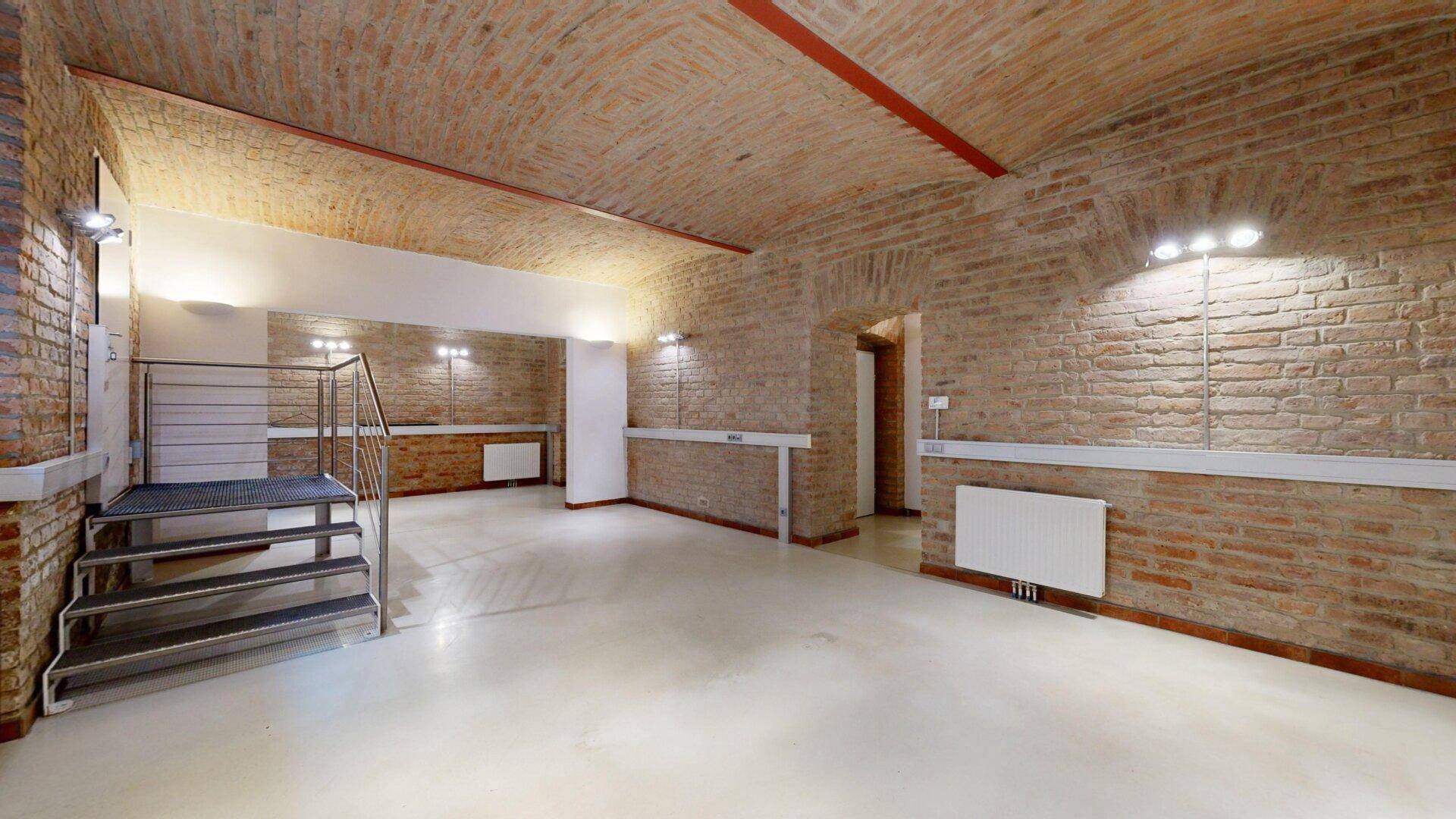 Großer Büroraum mit Ziegelwänden, Gewölbedecke und einem erhöhten Bereich mit Treppe.