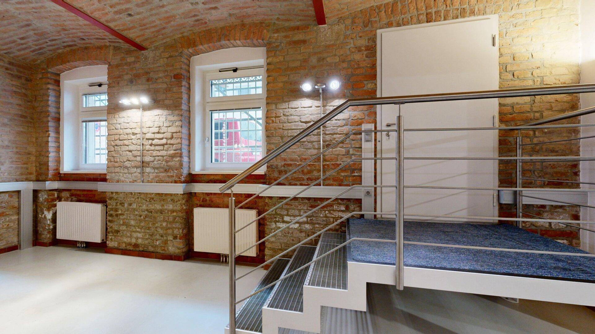Geräumiger Büroraum mit Ziegelwänden, Gewölbedecke und einer erhöhten Plattform mit Treppe.