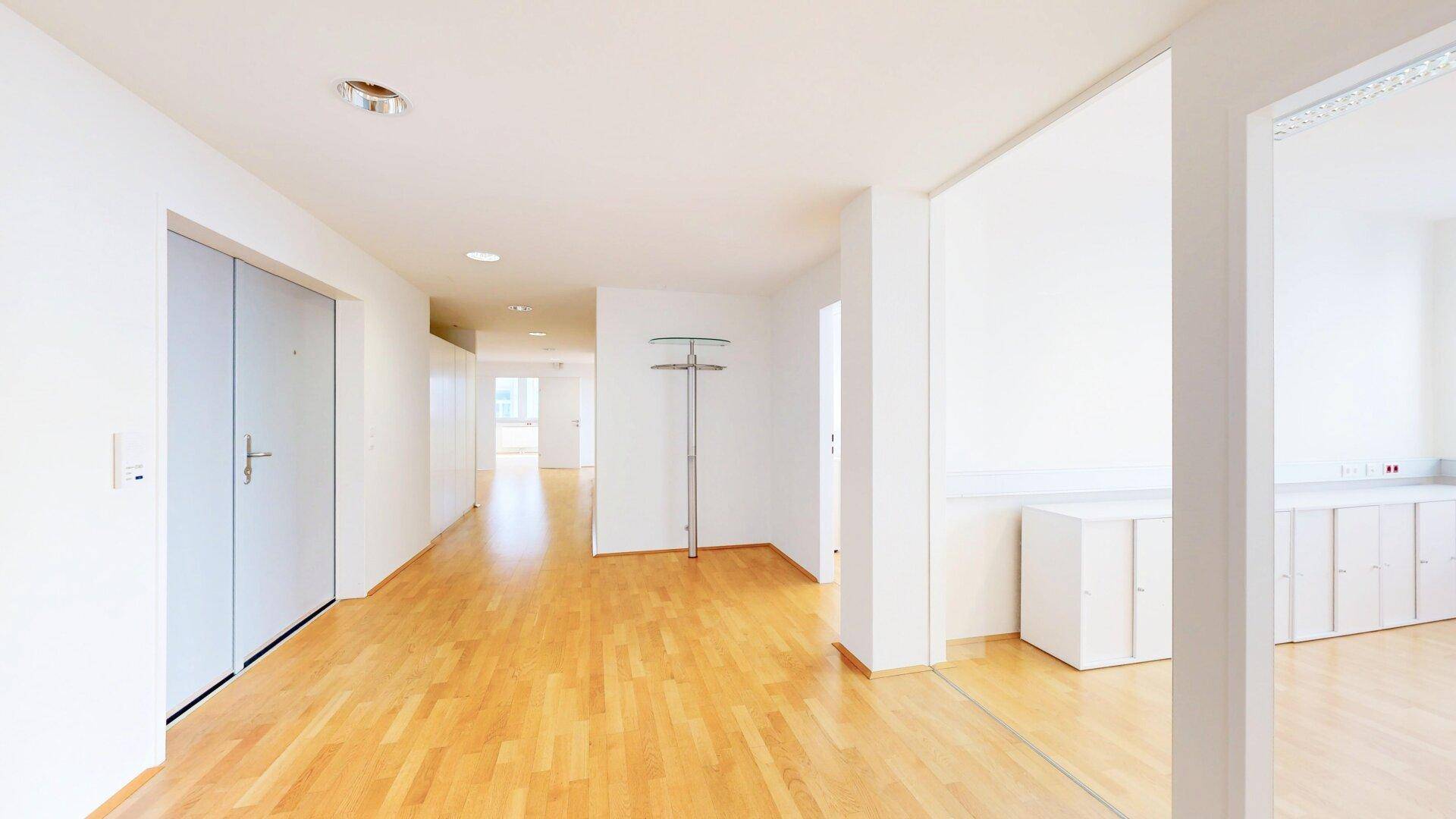 Heller Flur mit Holzfußboden, Garderobe und weißen Schränken, der zu weiteren Räumen führt.