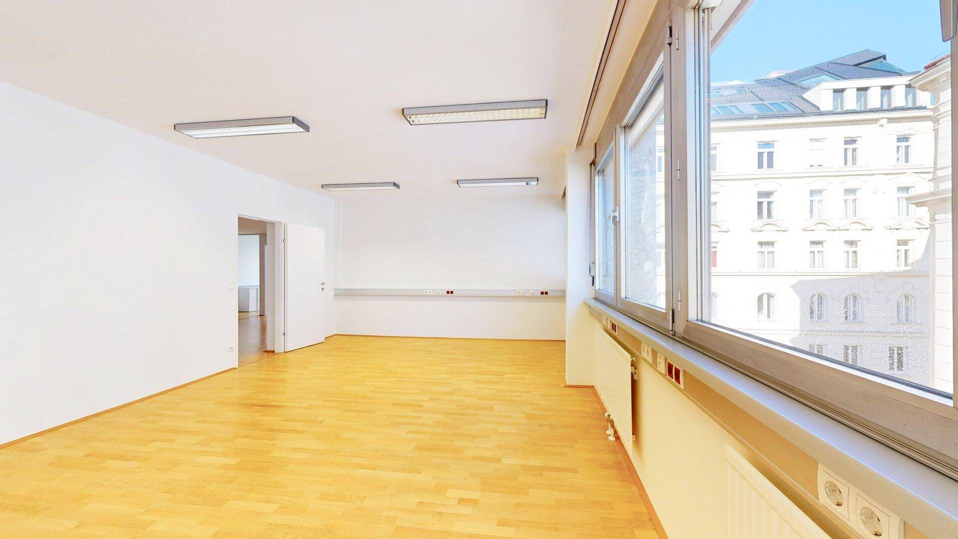 Geräumiges, leeres Büro mit großen Fenstern, die viel Tageslicht hereinlassen und Stadtblick bieten.