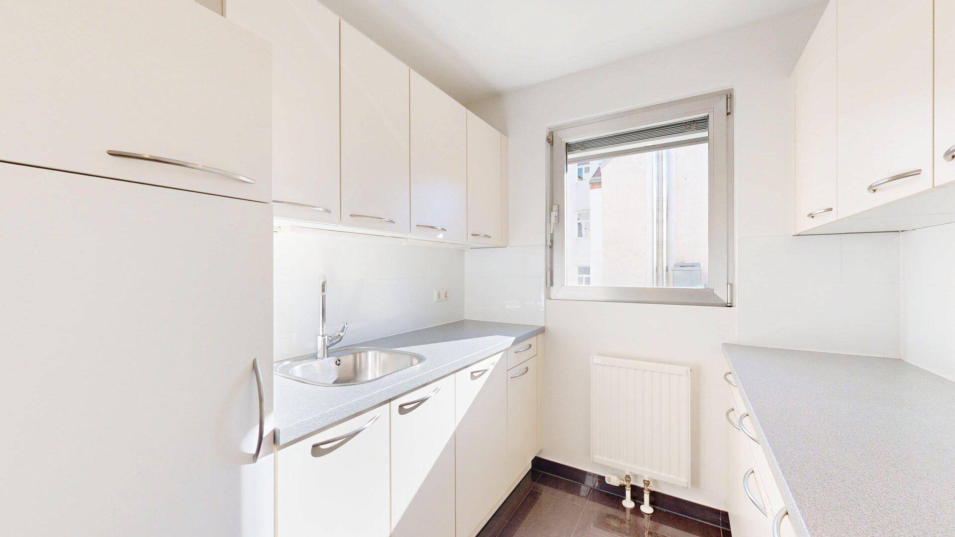 Funktionale Küchenzeile mit weißen Schränken, Spüle, Kühlschrank und Kaffeemaschine, mit Fenster.