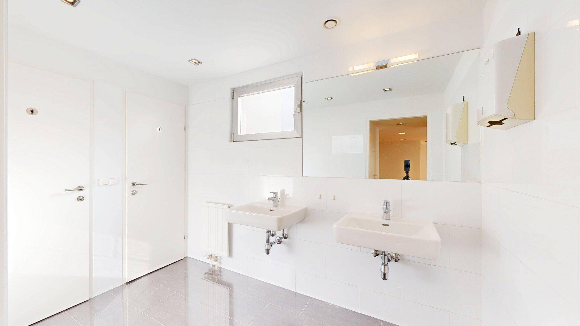 Helles Badezimmer mit zwei Waschbecken, großem Spiegel und Fenster, in modernem Design.