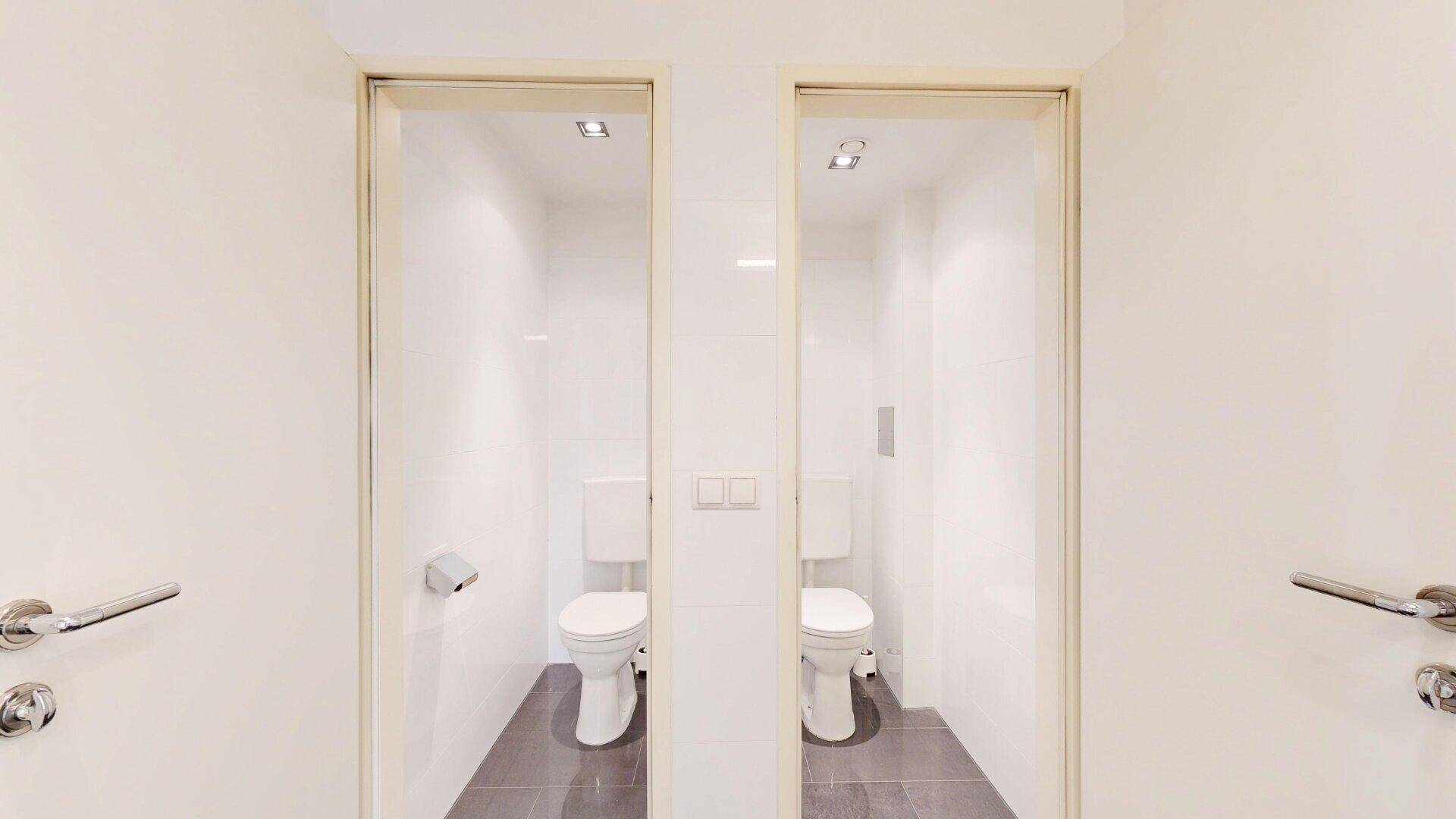 Zwei separate Toilettenräume mit weißen Fliesen und modernen WCs, zugänglich durch schlichte Türen.