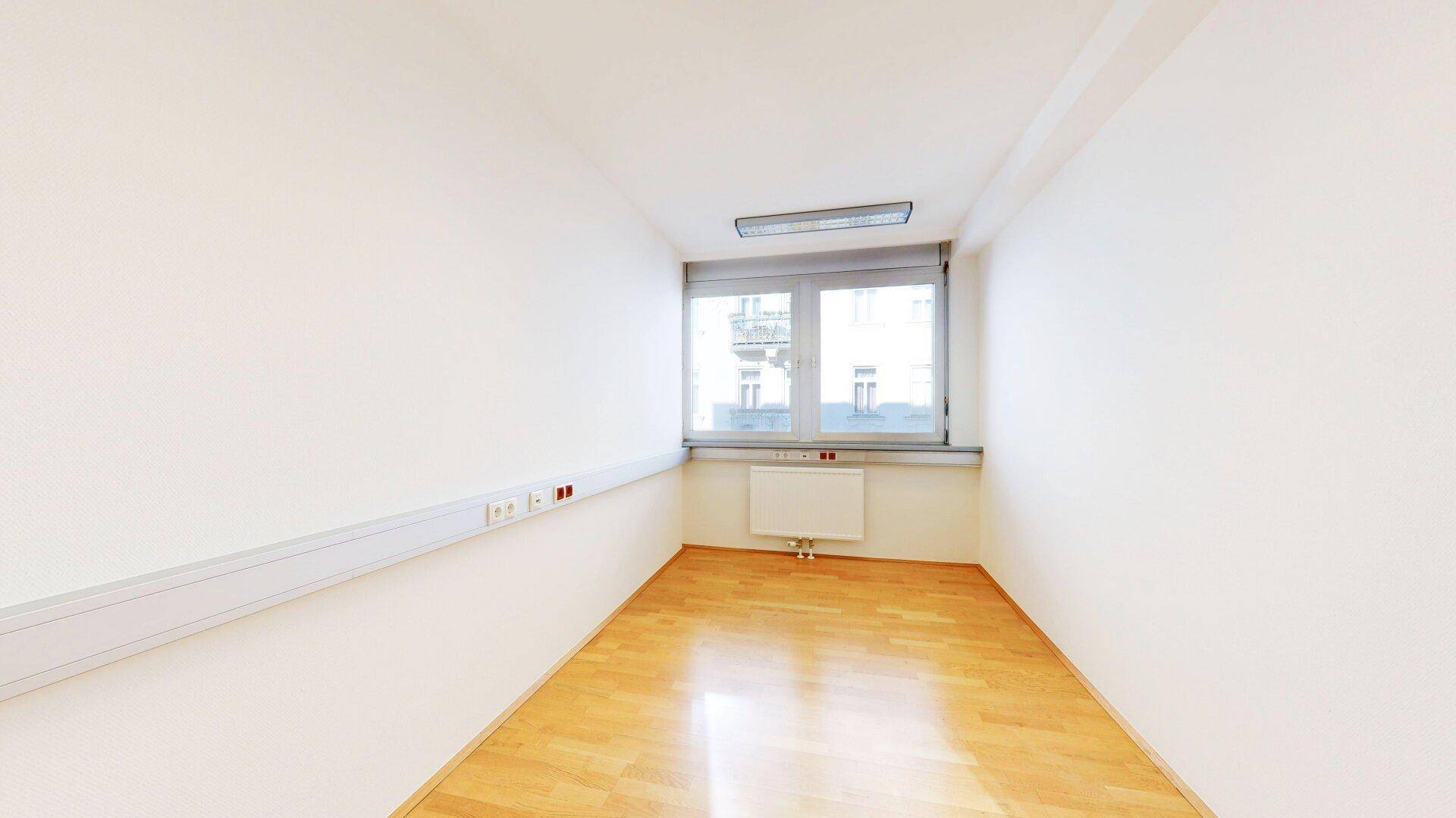 Leeres, helles Einzelbüro mit Fenster, Heizkörper und Holzfußboden, bereit zur individuellen Gestaltung.