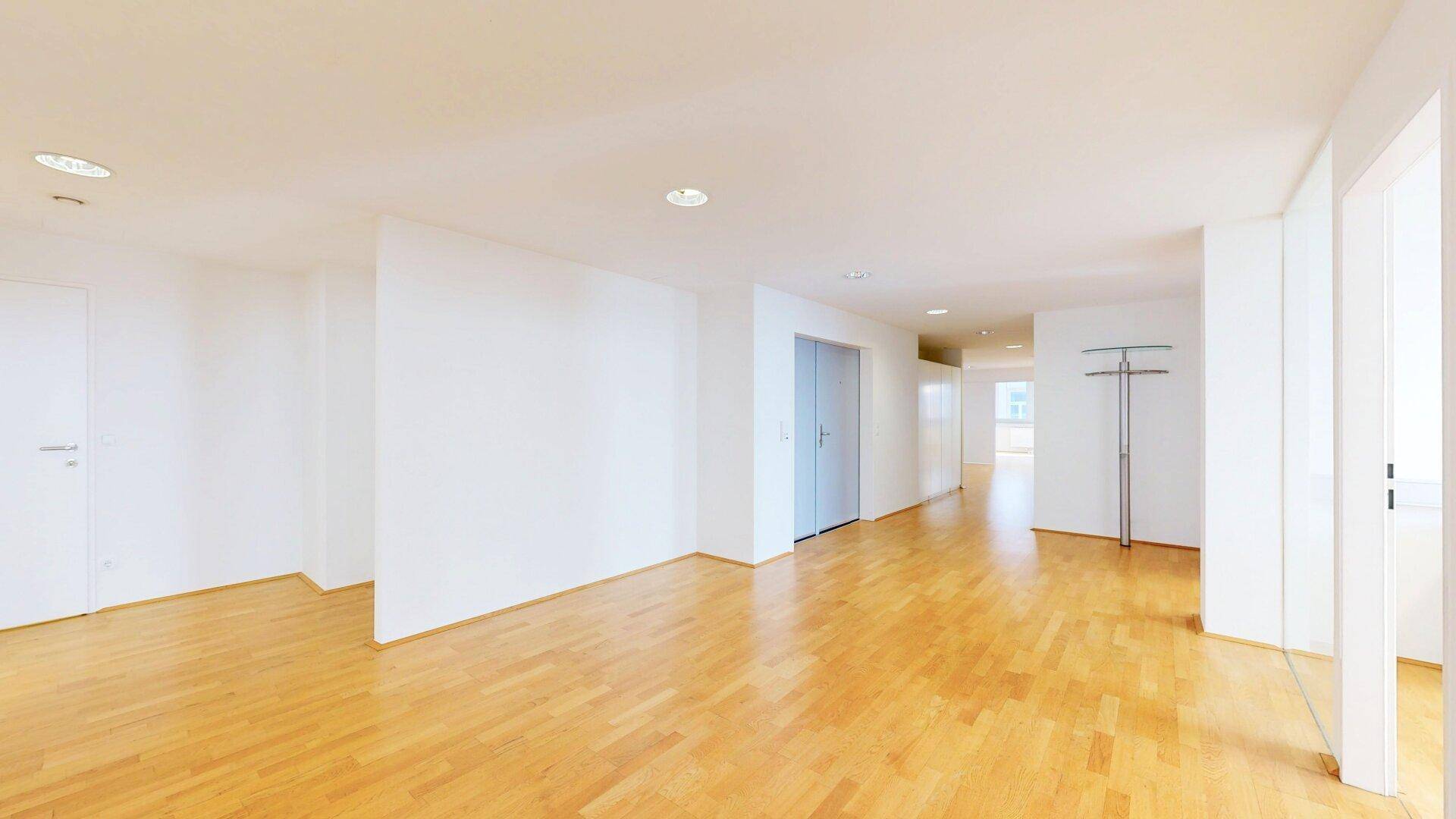 Leerer, heller Flur mit Holzfußboden und weißen Wänden, der zu weiteren Räumen führt.