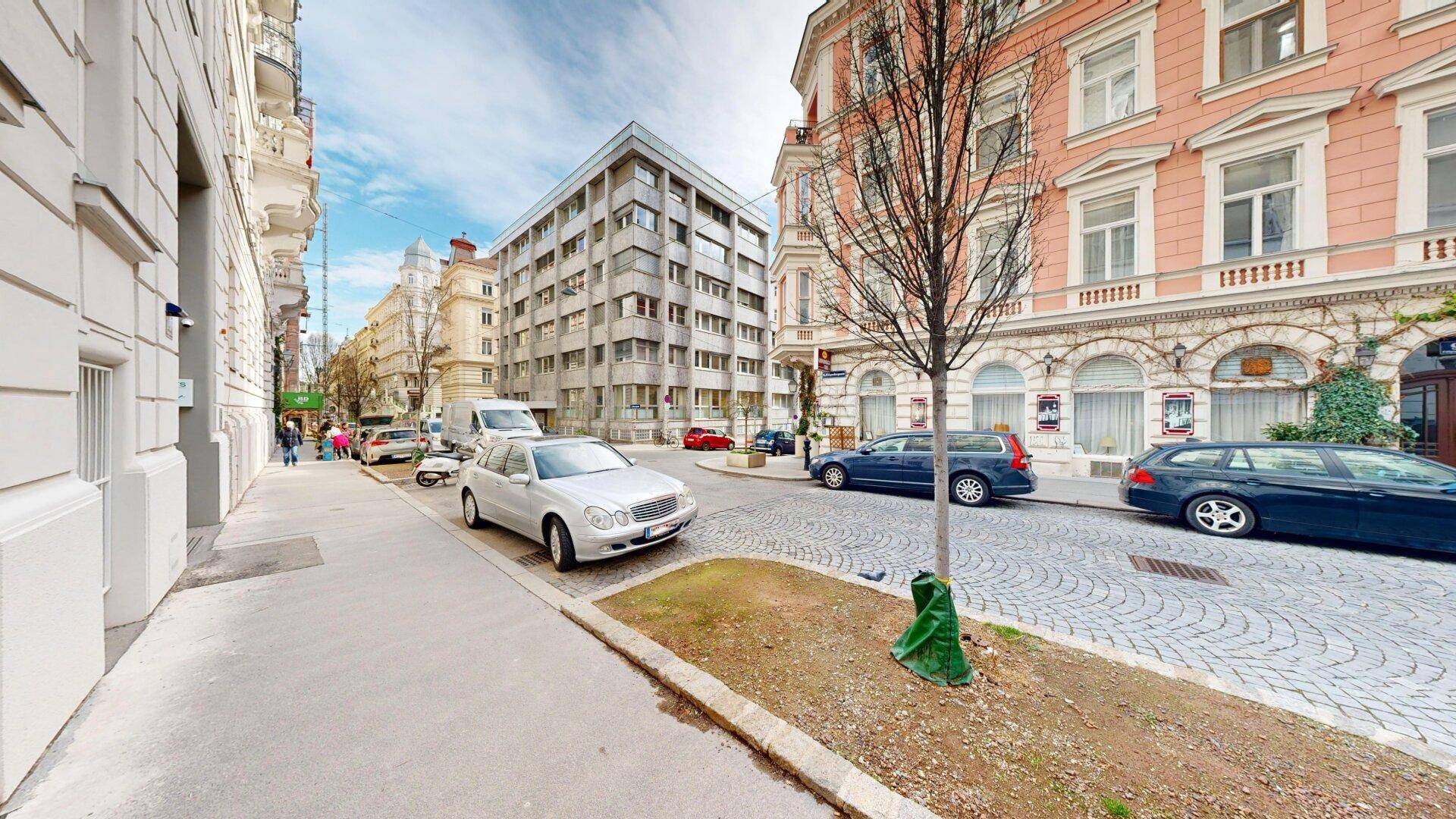 Eine belebte Straße mit geparkten Autos und historischen Gebäuden unter einem blauen Himmel.