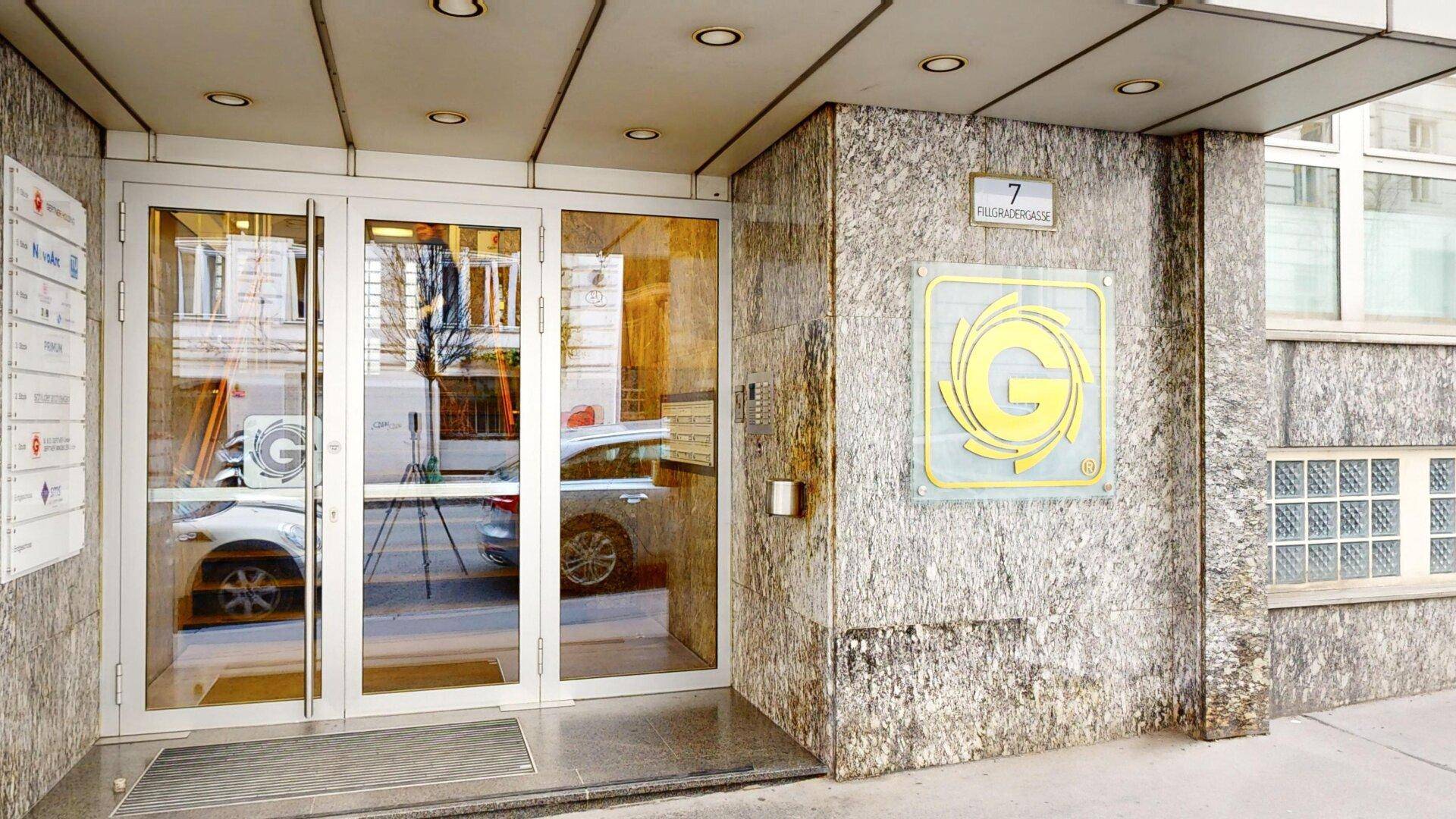 Moderner Gebäudeeingang mit Glasfront und Marmorverkleidung, inklusive Firmenlogo und Hausnummer.