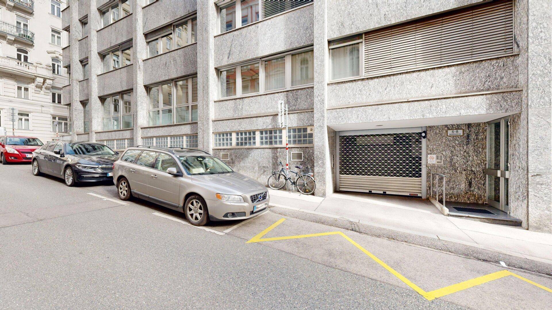 Gebäudefassade mit strukturiertem Putz und einem Garagentor, daneben ein Fahrrad und geparkte Autos.