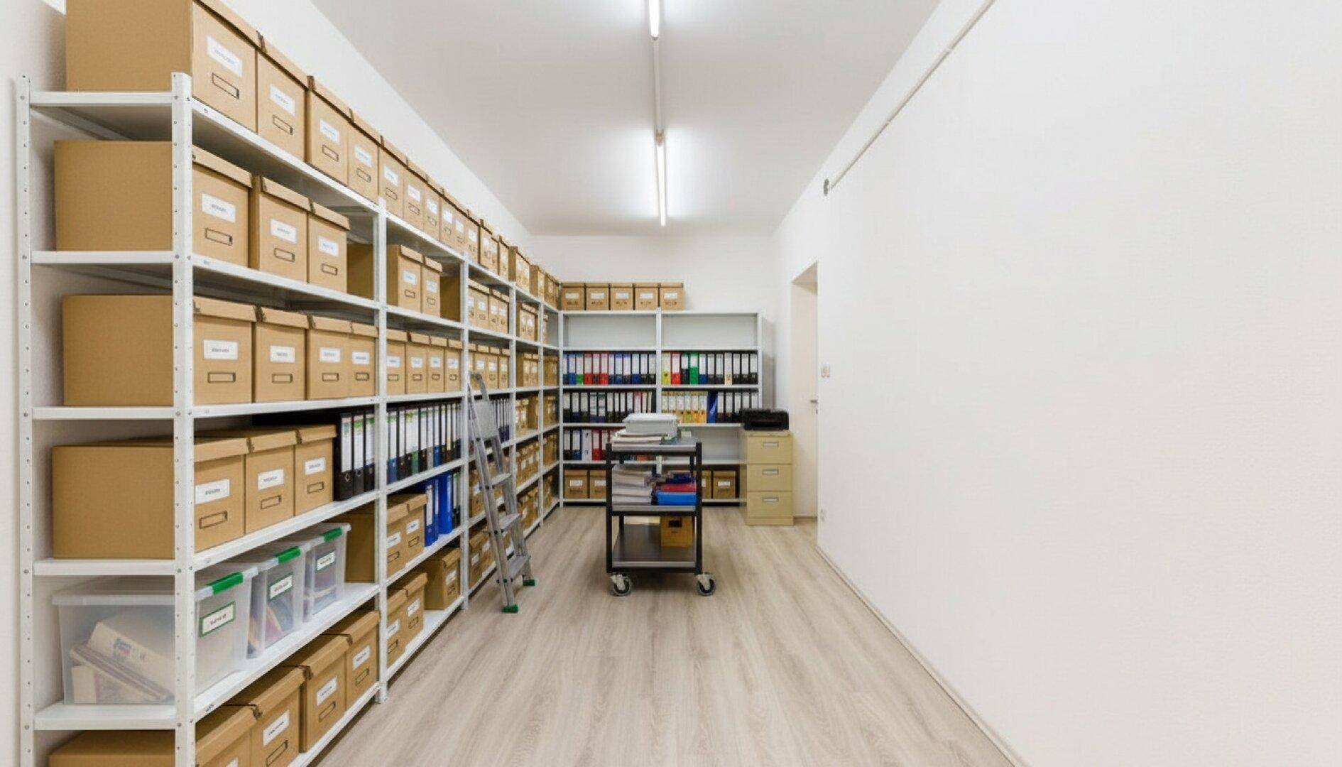 Umfangreicher Archivraum mit hohen Metallregalen, gefüllt mit Aktenordnern und Kartons, auf hellem Laminatboden.