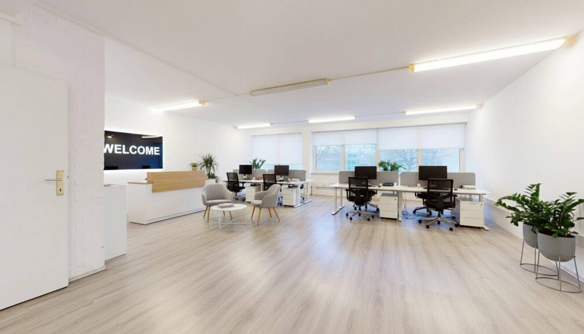 Modernes Großraumbüro mit Empfangsbereich, mehreren Arbeitsplätzen und viel Tageslicht.