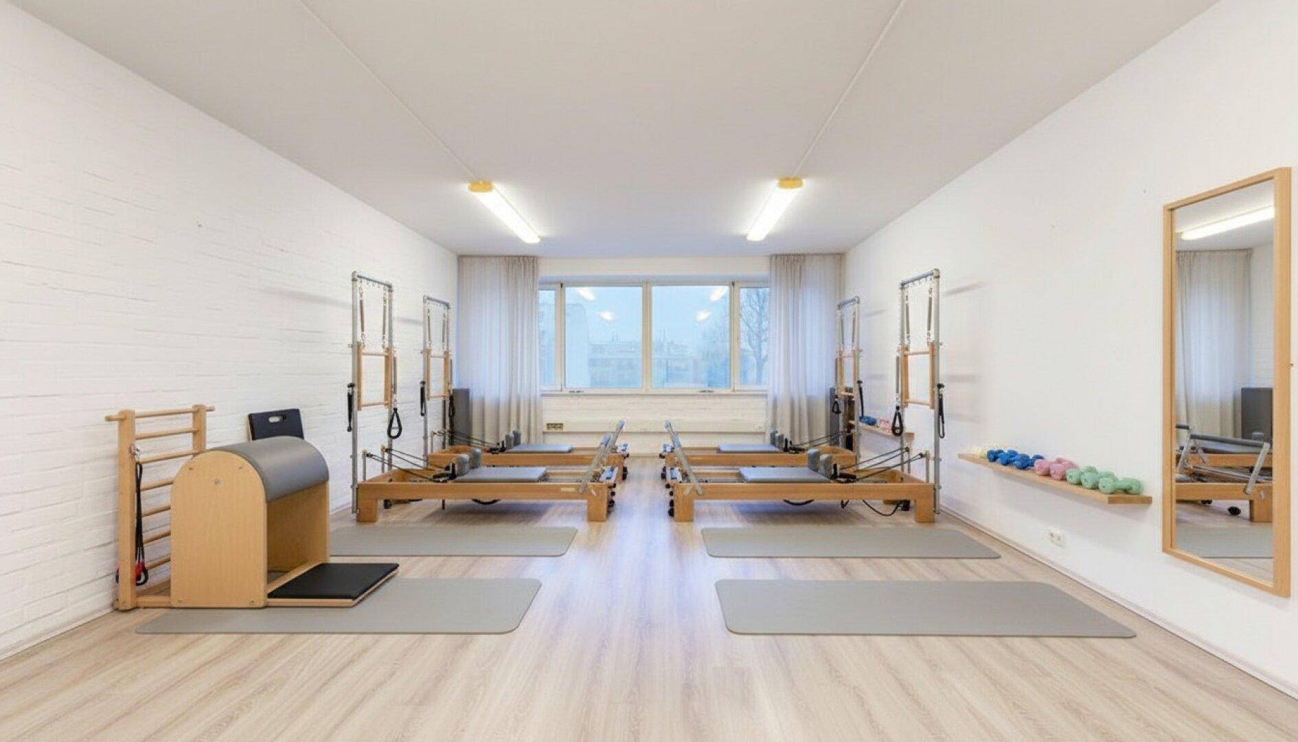 Modernes Pilates-Studio mit mehreren Reformern, Spiegeln und großen Fenstern für Training.