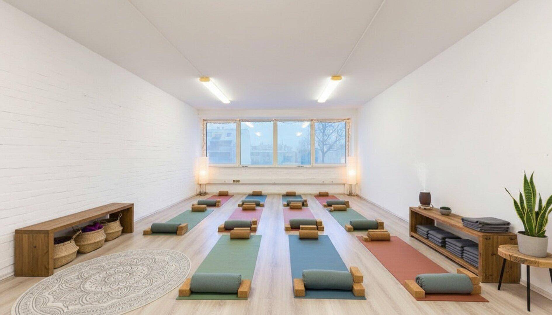 Geräumiger Yogaraum mit Matten, Holzbänken und viel Tageslicht, ideal für Gruppenkurse.