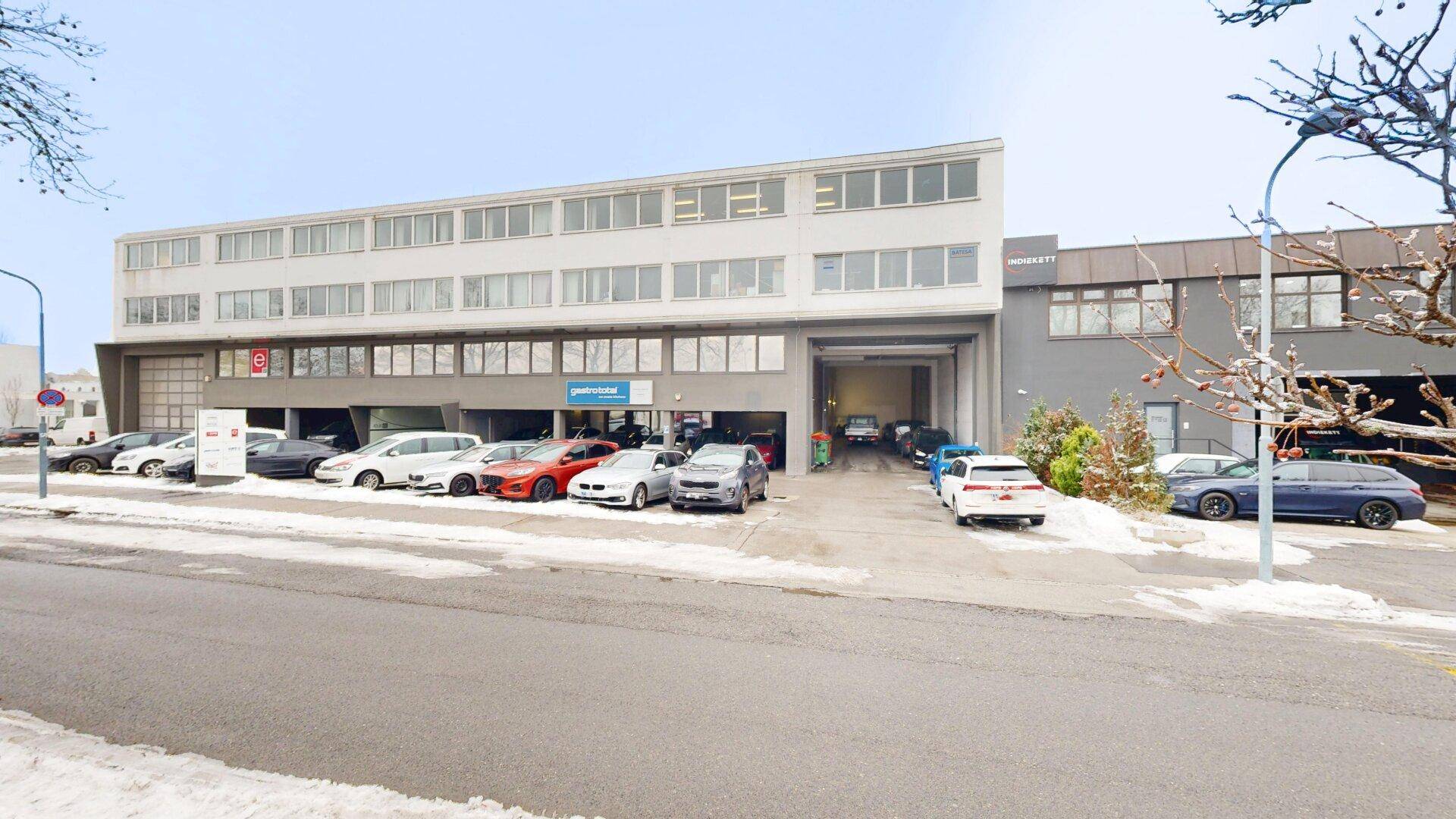 Modernes Geschäftsgebäude mit mehreren Etagen, großen Fenstern und einem Parkplatz davor, umgeben von Schnee.