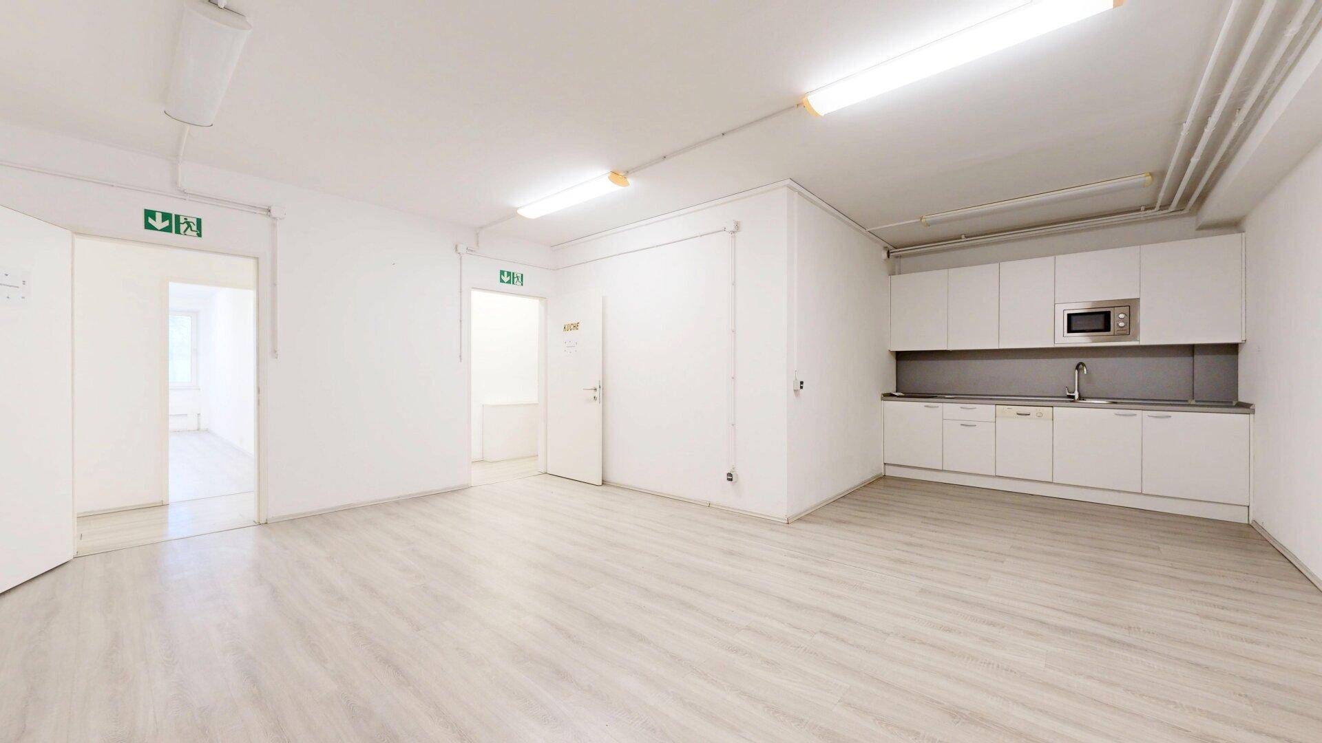 Funktionale Küchenzeile mit weißen Schränken und Mikrowelle in einem hellen Raum mit Laminatboden und mehreren Türen.