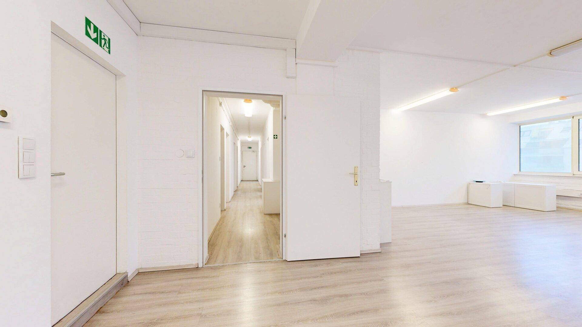 Heller Flurbereich mit mehreren Türen und einem langen Korridor im Hintergrund, ausgestattet mit Laminatboden.